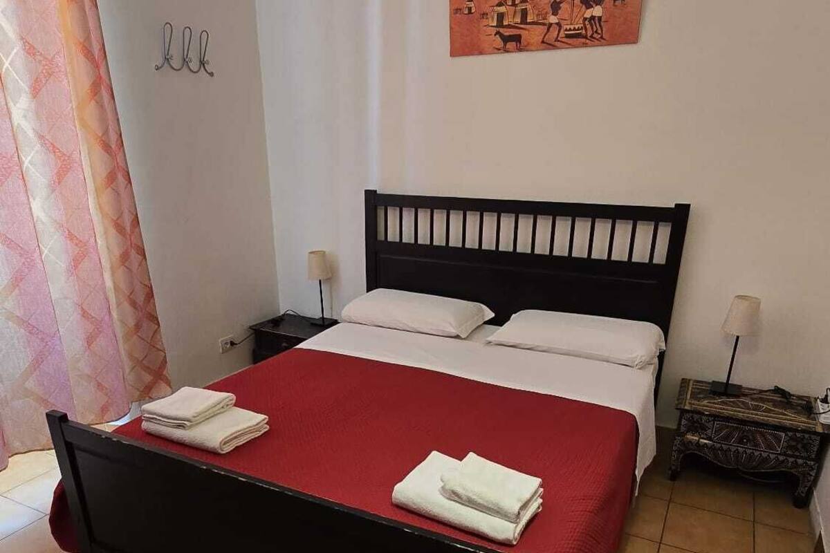 A neatly made bed with red bedding and white pillows, a black headboard, and a small bedside table with a lamp.