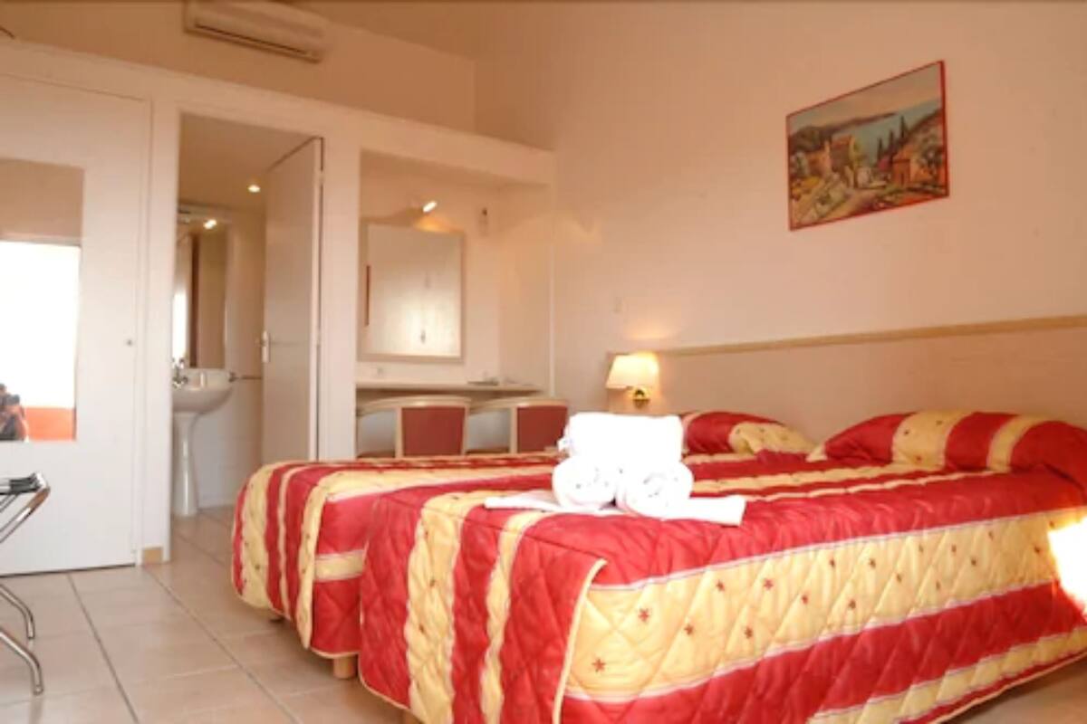 A hotel room with two beds, a desk, and a bathroom.