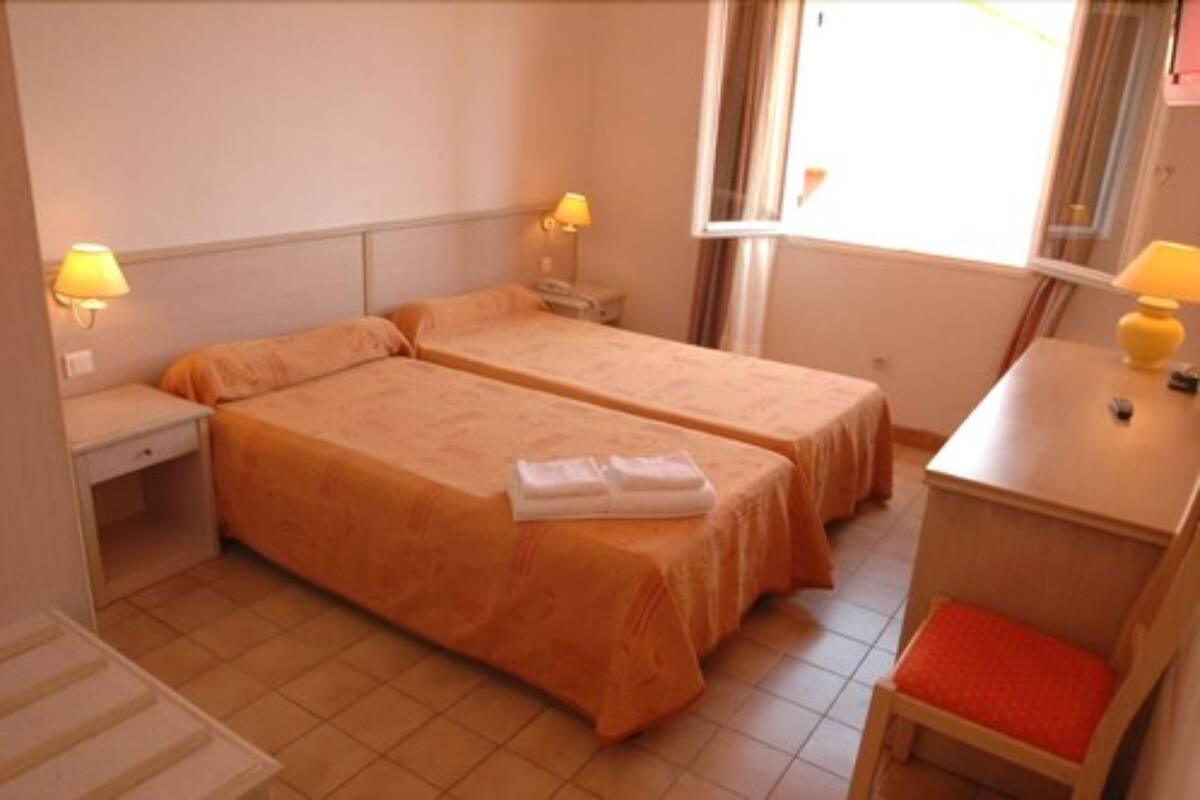 A hotel room with two beds, a desk, a chair, and a window.
