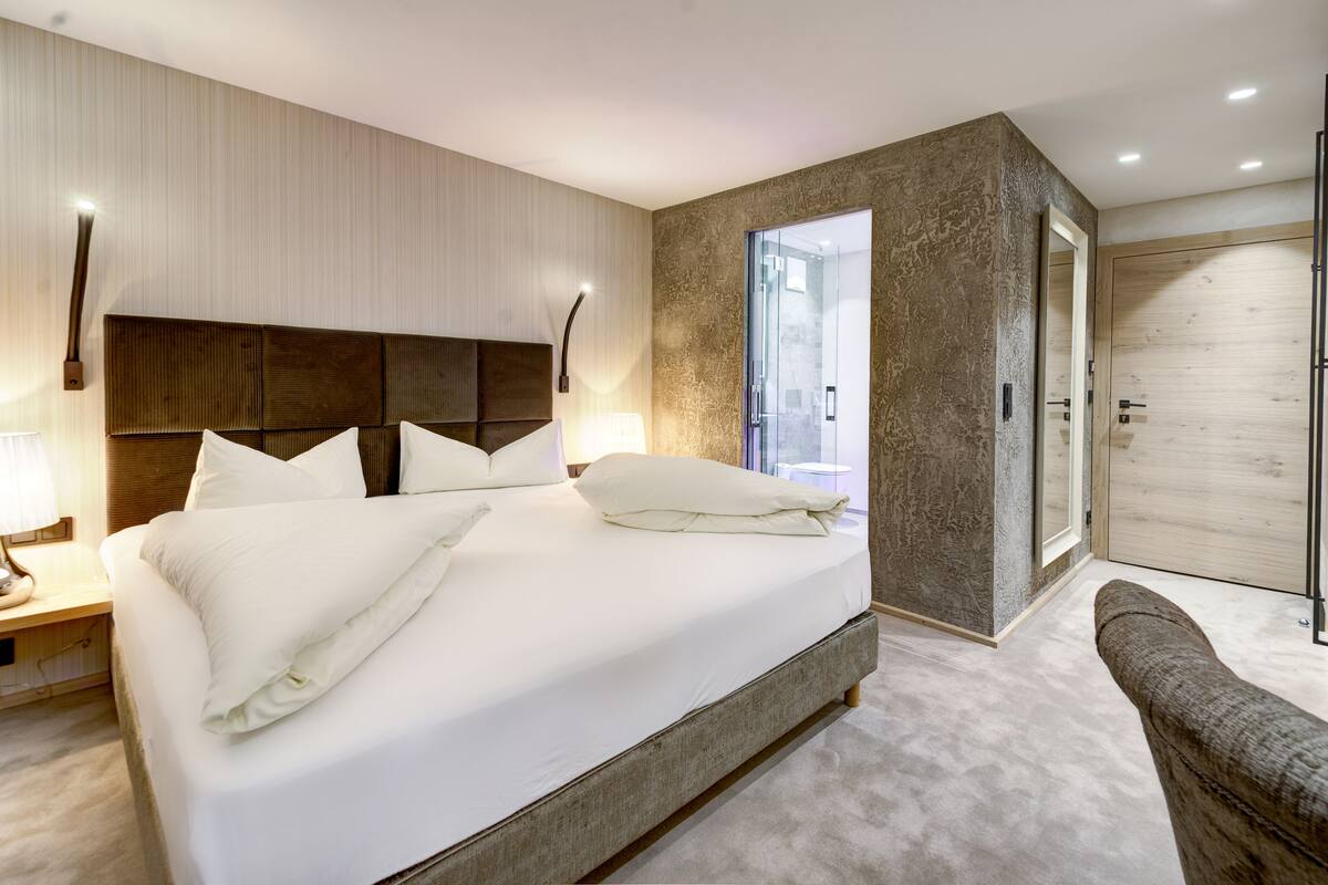 A modern bedroom with a large bed, a bedside table, a chair, and a walk-in closet.