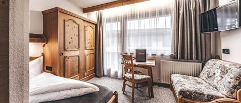 Un dormitorio con una cama, un armario de madera, un escritorio con una silla, un sofá y un televisor montado en la pared.