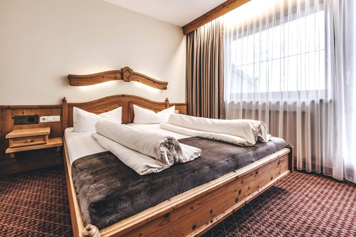 A hotel room with a wooden bed, a nightstand, and a large window with curtains.
