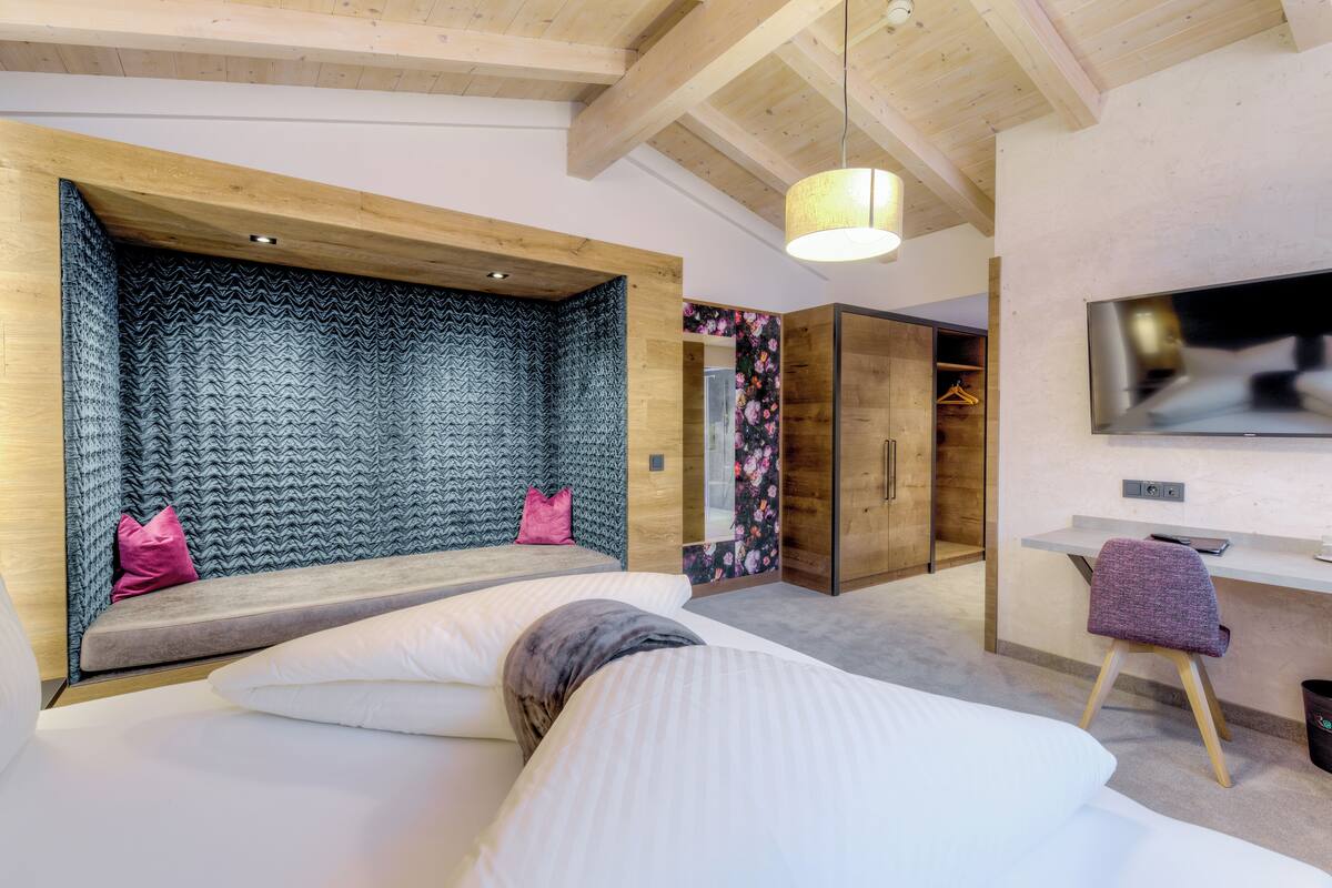 A modern bedroom with a large bed, a built-in bench, a desk, and a TV.