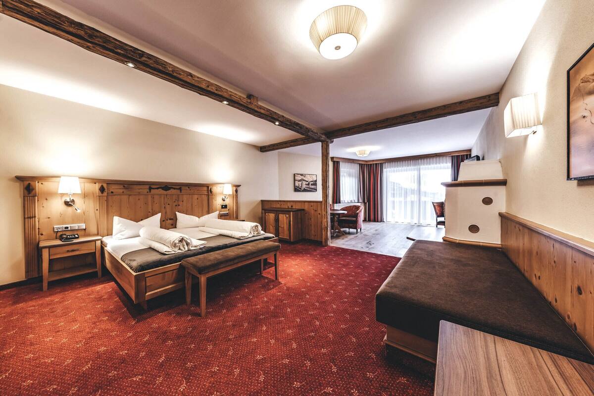 A hotel room with a large bed, a wooden bench, a desk, and a view of the outdoors.