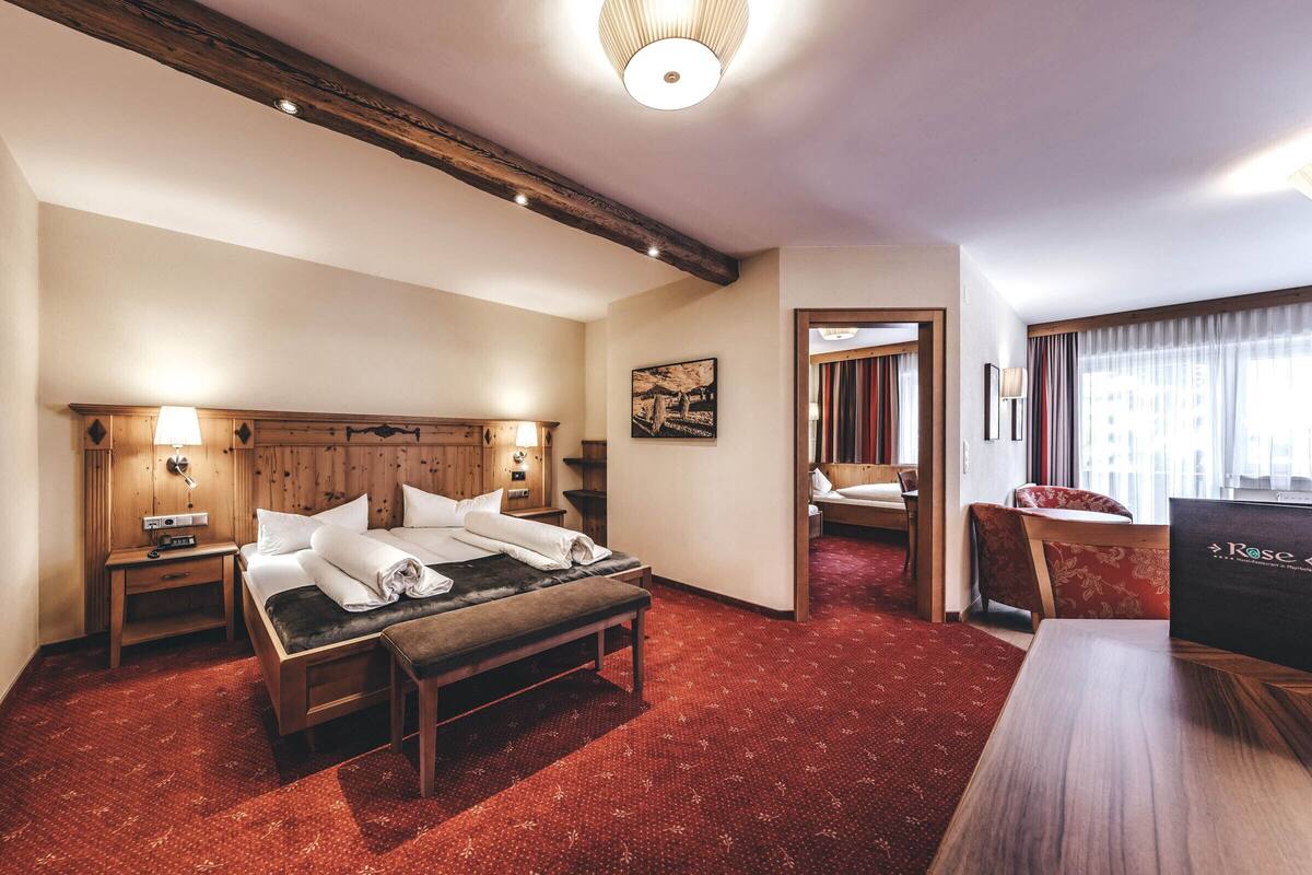 A hotel room with a wooden bed, a bench, a desk, and a mirror.