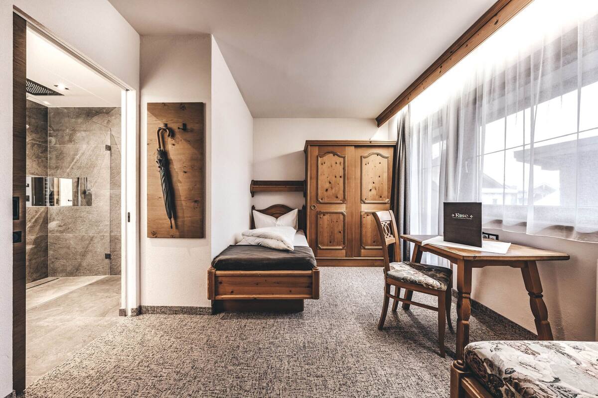 A bedroom with a bed, a wooden desk, a chair, a wardrobe, and a shower area.