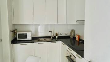 Una pequeña cocina con armarios blancos, encimera negra, microondas, lavabo y estufa.