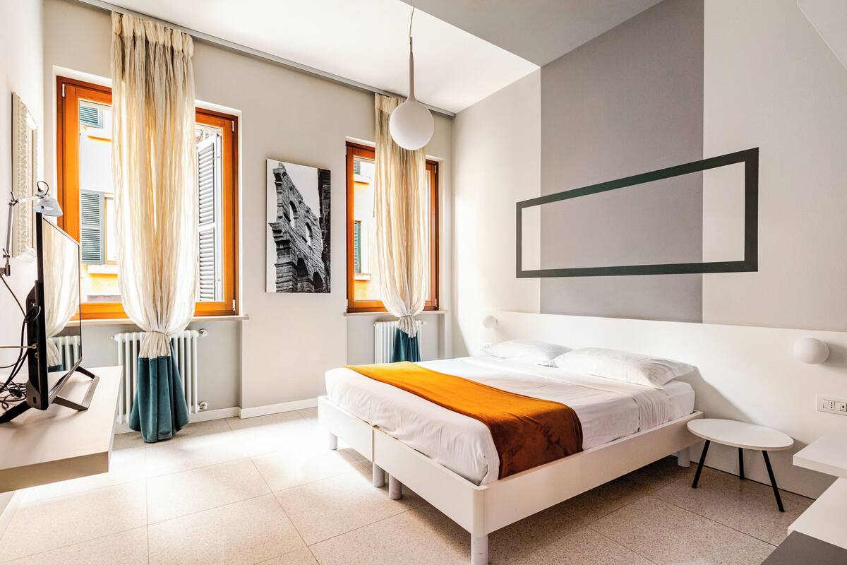 A modern bedroom with a bed, bedside table, and a view of the outside through large windows.