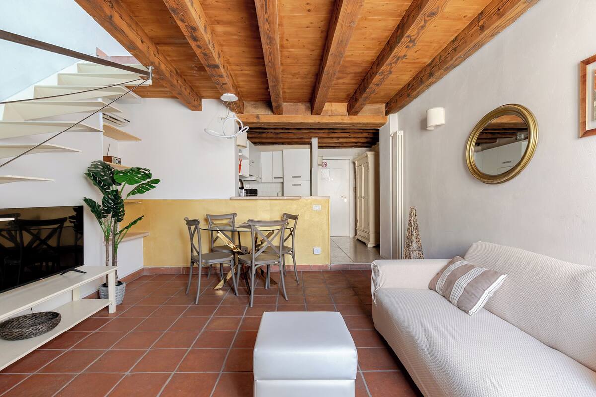 A modern living space with a staircase, a dining area, a sofa, and a kitchen.