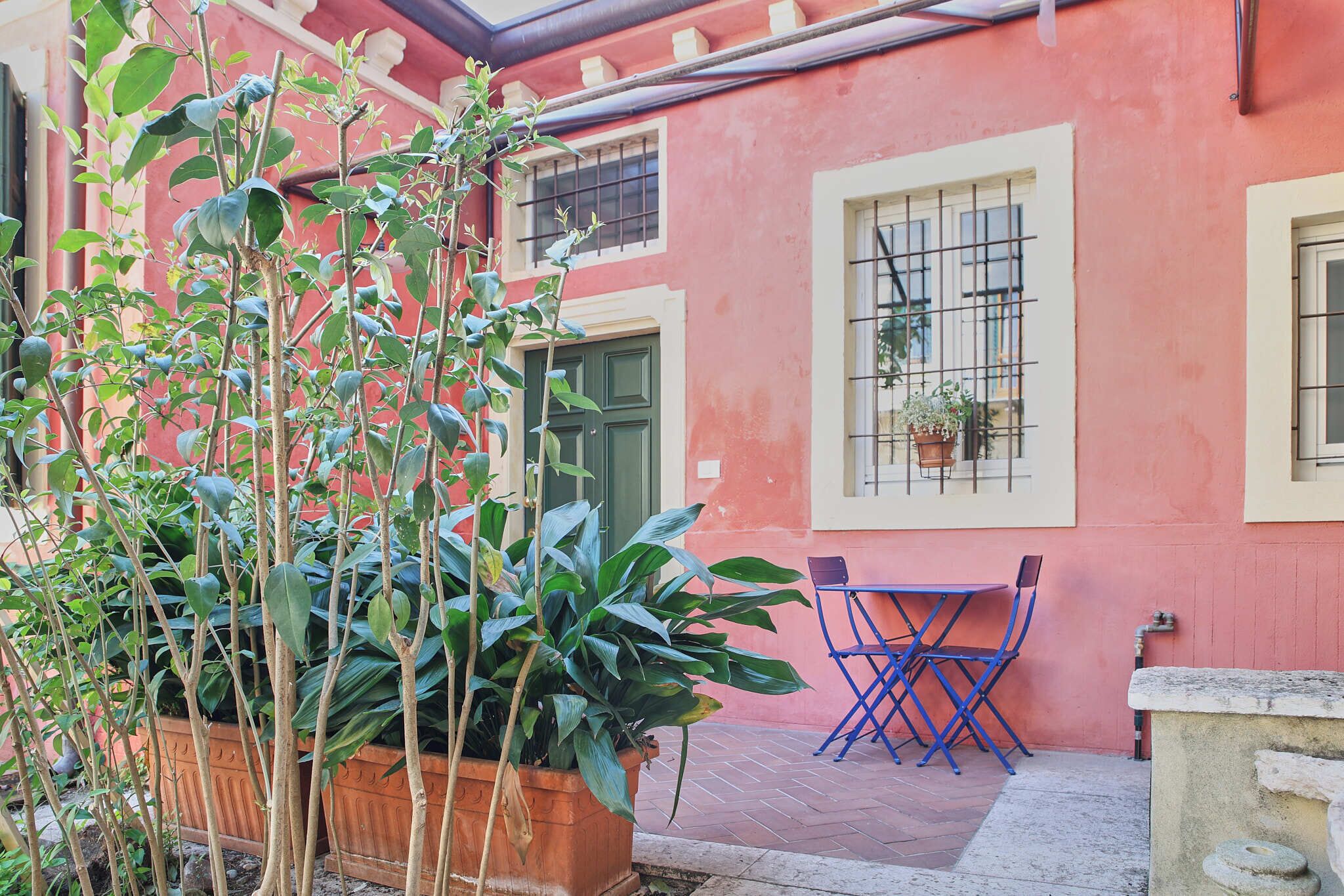 A red building with a green door, a window with a metal grill, and a blue folding table with chairs.