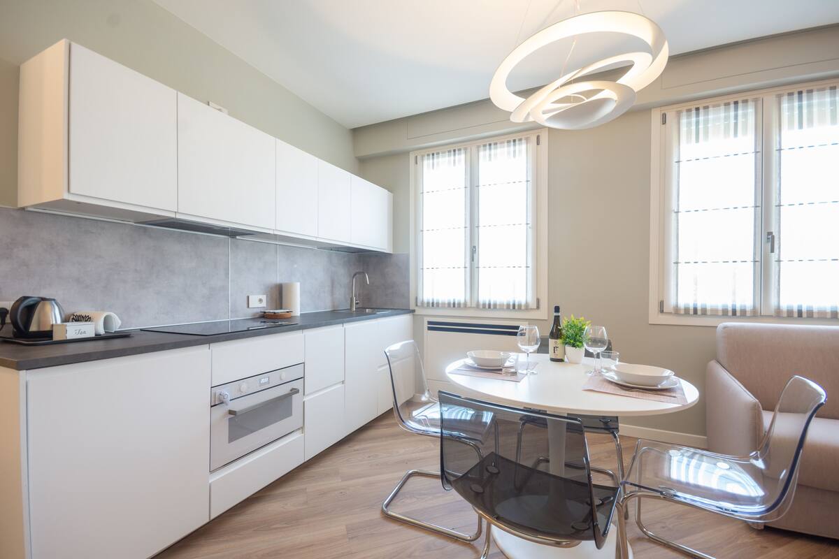 A modern kitchen with white cabinets, a built-in oven, and a dining area with a round table and chairs.