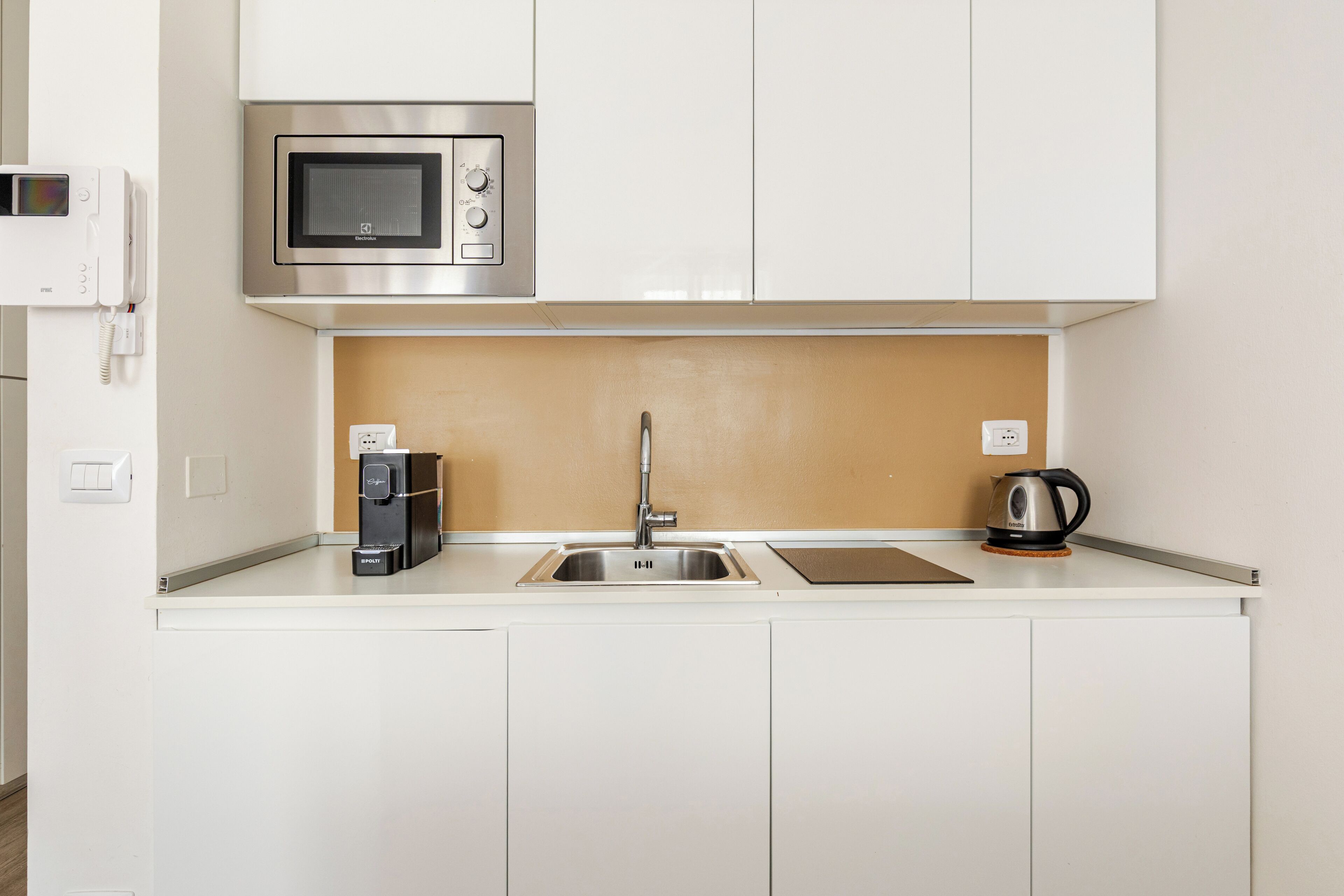 A kitchenette with a microwave, coffee maker, kettle, and a sink.