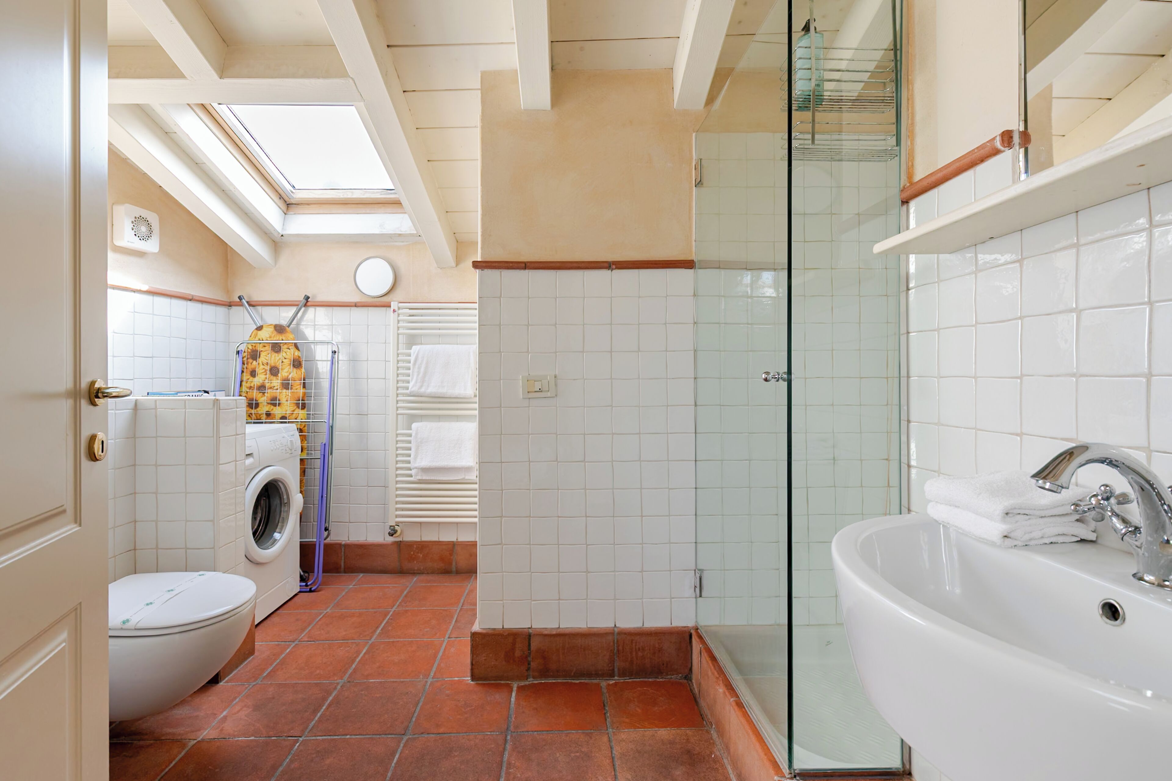 A bathroom with a washing machine, a glass shower enclosure, and a sink.