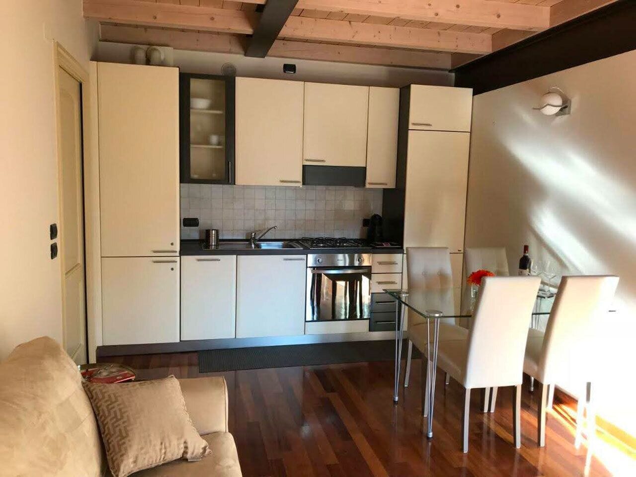 Une cuisine moderne avec des meubles blancs, un coin repas doté d’une table et de chaises en verre, et un plafond en bois.
