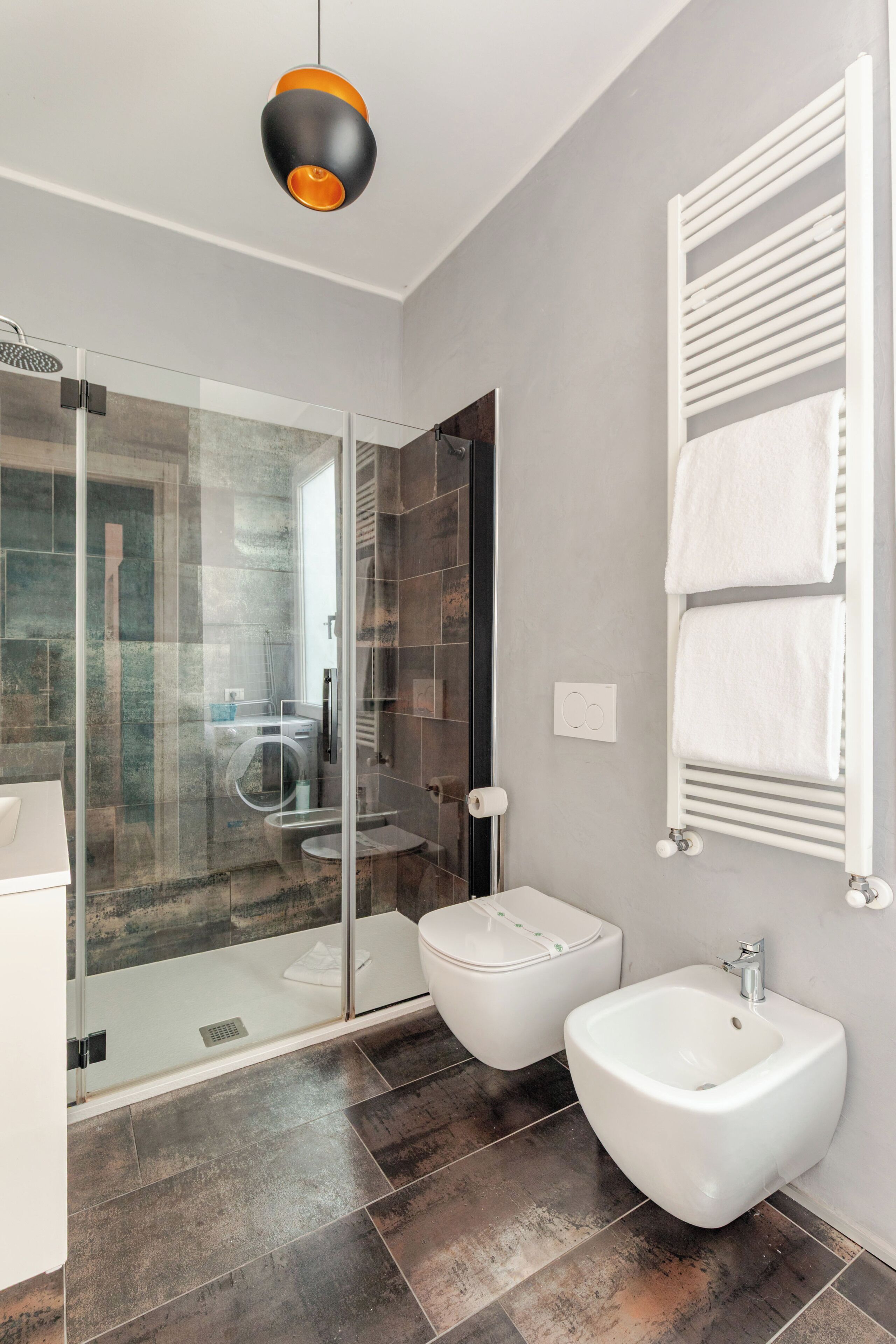 A modern bathroom with a glass shower enclosure, a bidet, a white sink, and a towel rack.