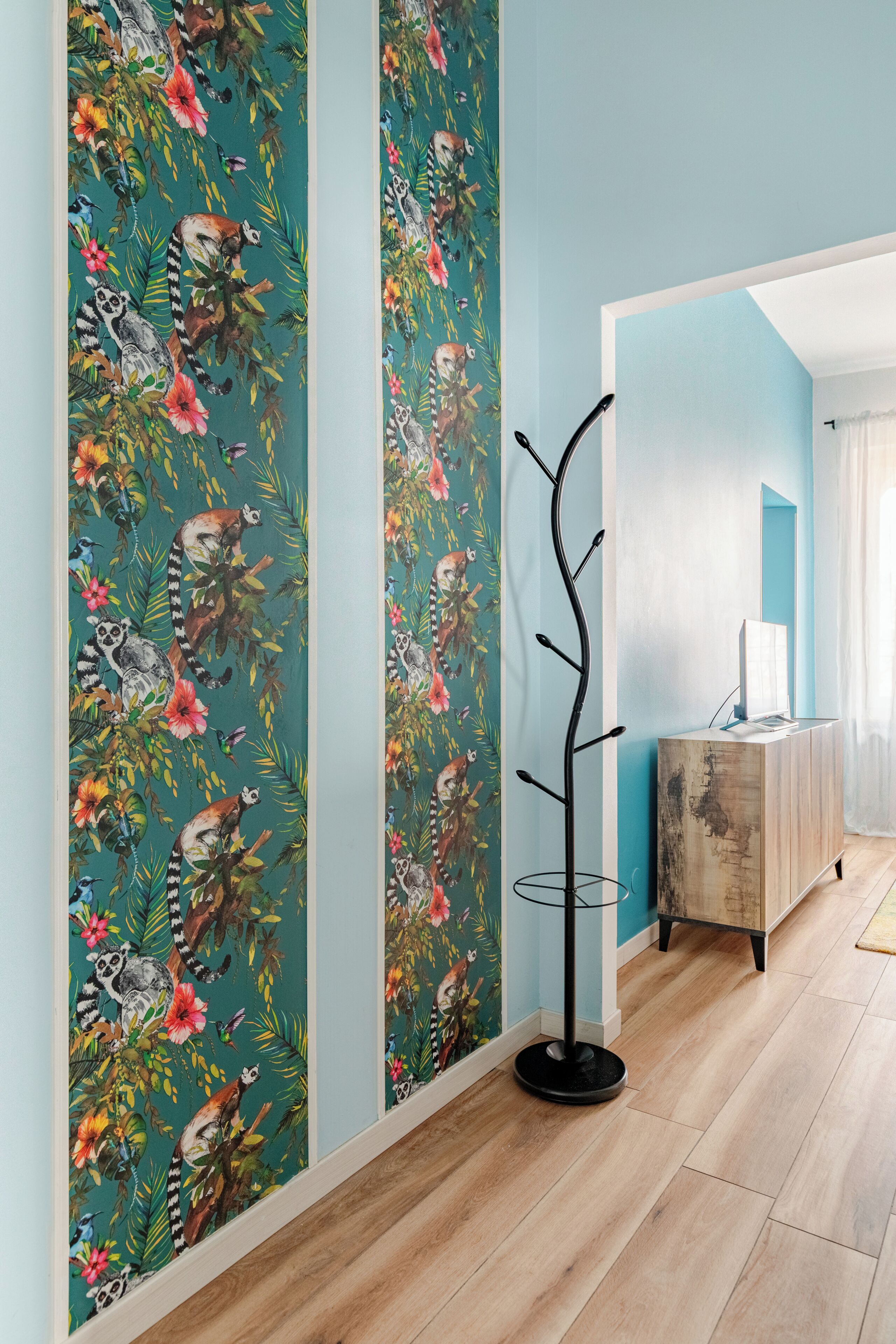 Passadís amb terra de fusta, una làmpada de peu negra i un mur amb paper tapet de fauna i flora tropical.