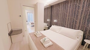 Habitación de hotel con cama, mesita de noche con toallas, espejo y pared decorada con un diseño de árbol.