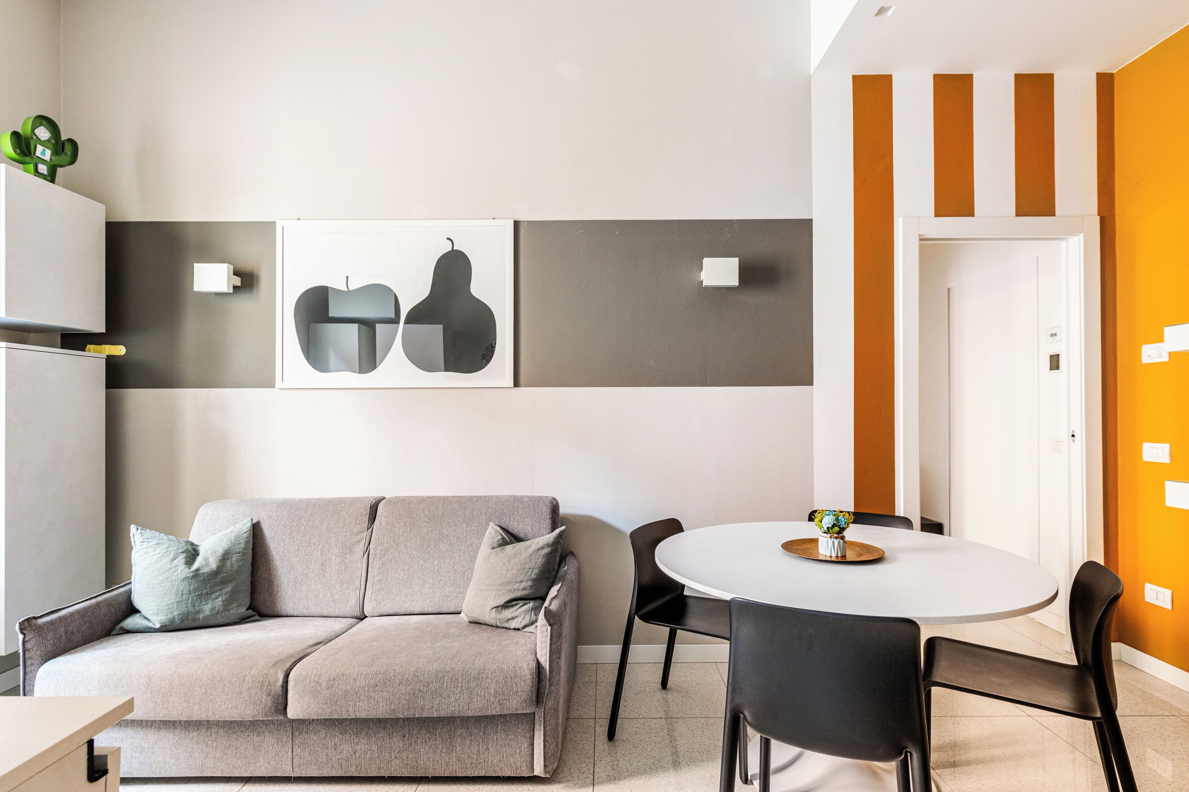 A modern living room with a sofa, chairs, a dining table, and artwork on the wall.