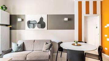 A modern living room with a sofa, chairs, a dining table, and artwork on the wall.