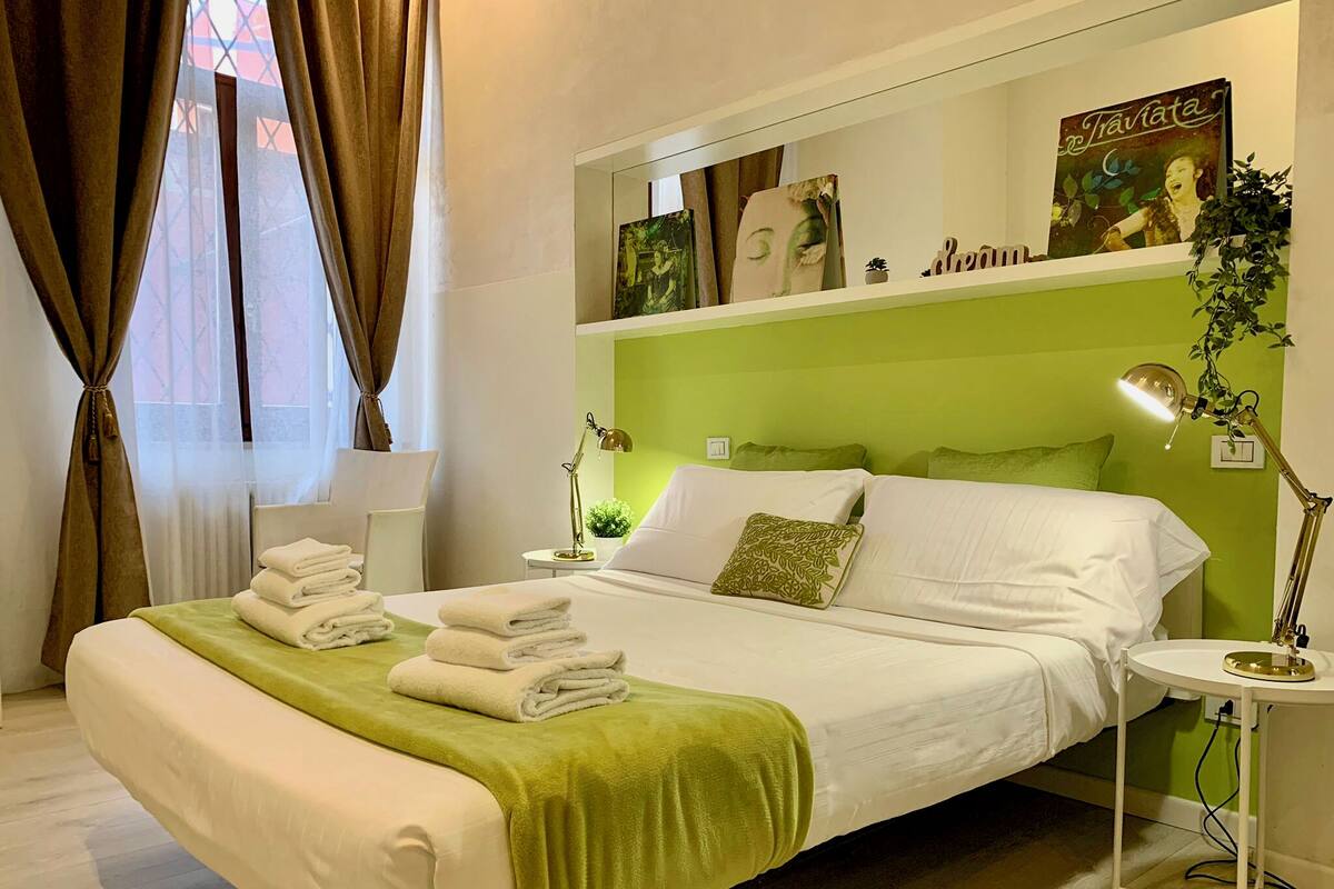 Una cama bien hecha con toallas dobladas, una lámpara de noche y una pared verde.