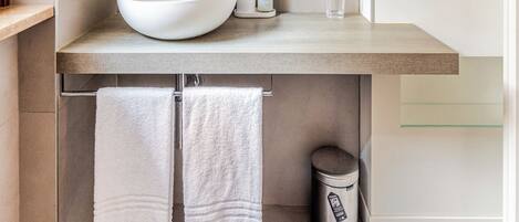A modern bathroom with a large white sink, a mirror, a towel rack, and macramé plant hangers.