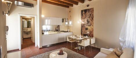 A modern kitchen with white cabinets, a dining area with a glass table, and a living room with a beige sofa.