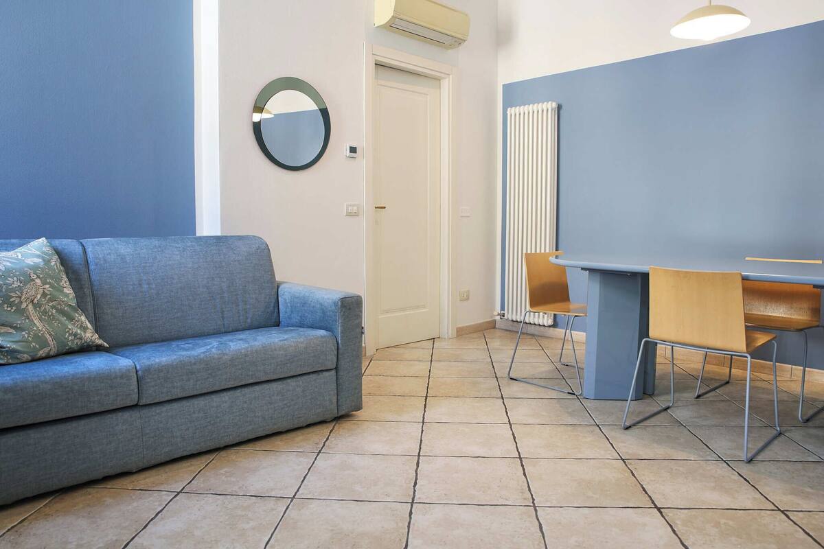 A room with a blue sofa, a dining table with chairs, a radiator, and a door.