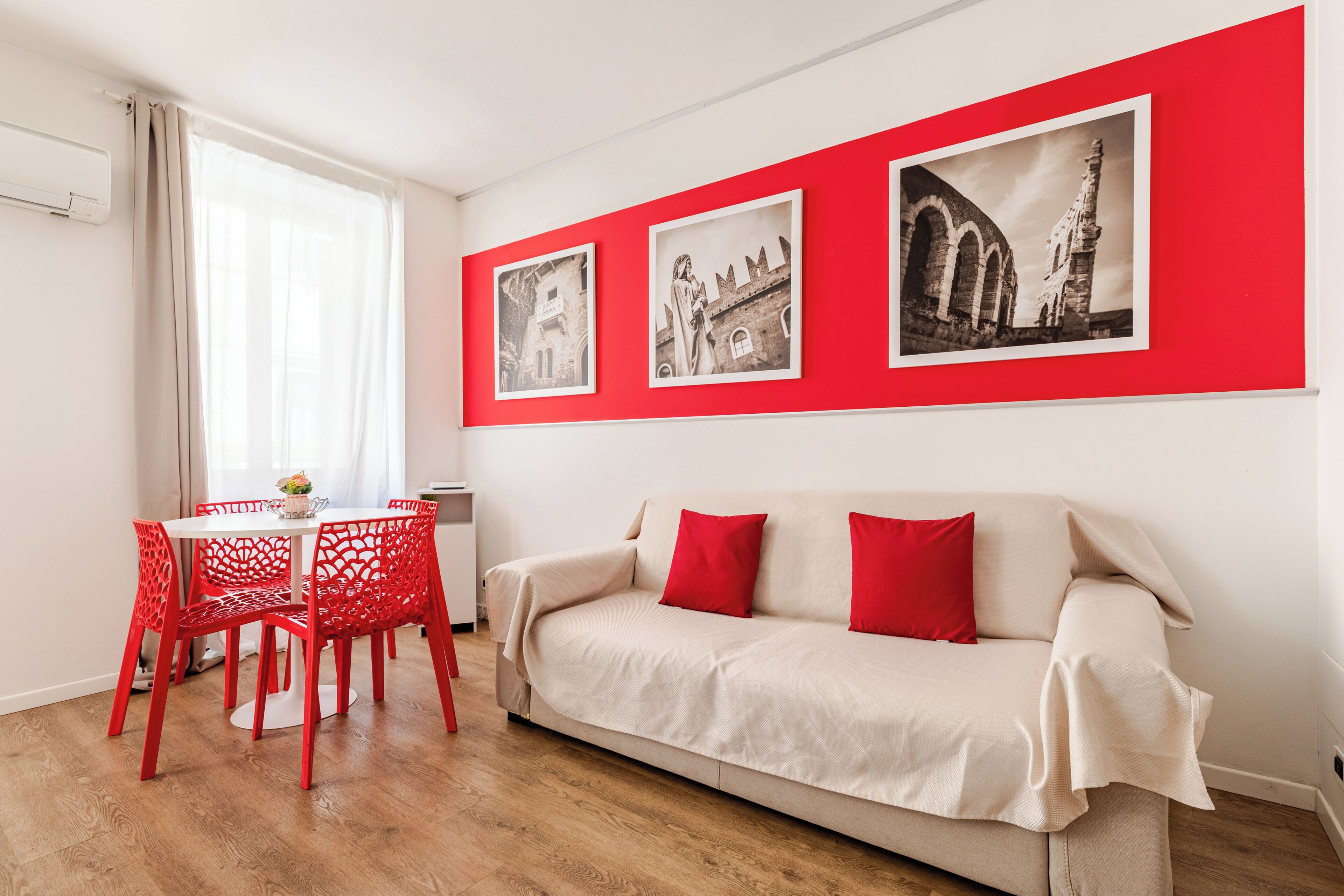 A room with a white sofa, red chairs, a dining table, and three black-and-white photographs on the wall.