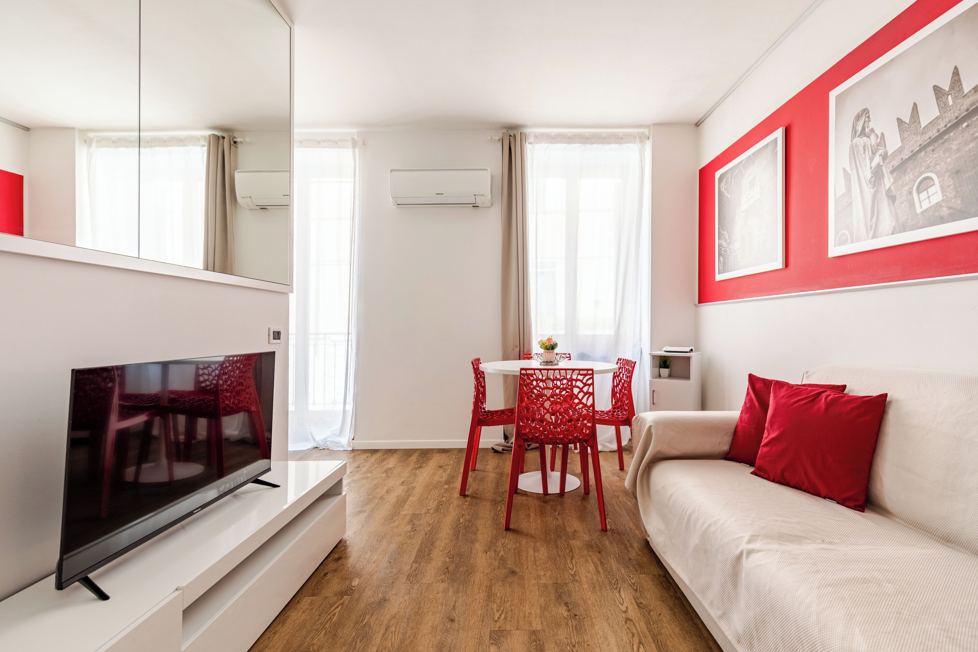 A modern living room with a flat-screen TV, red chairs, a white sofa, and a dining table.