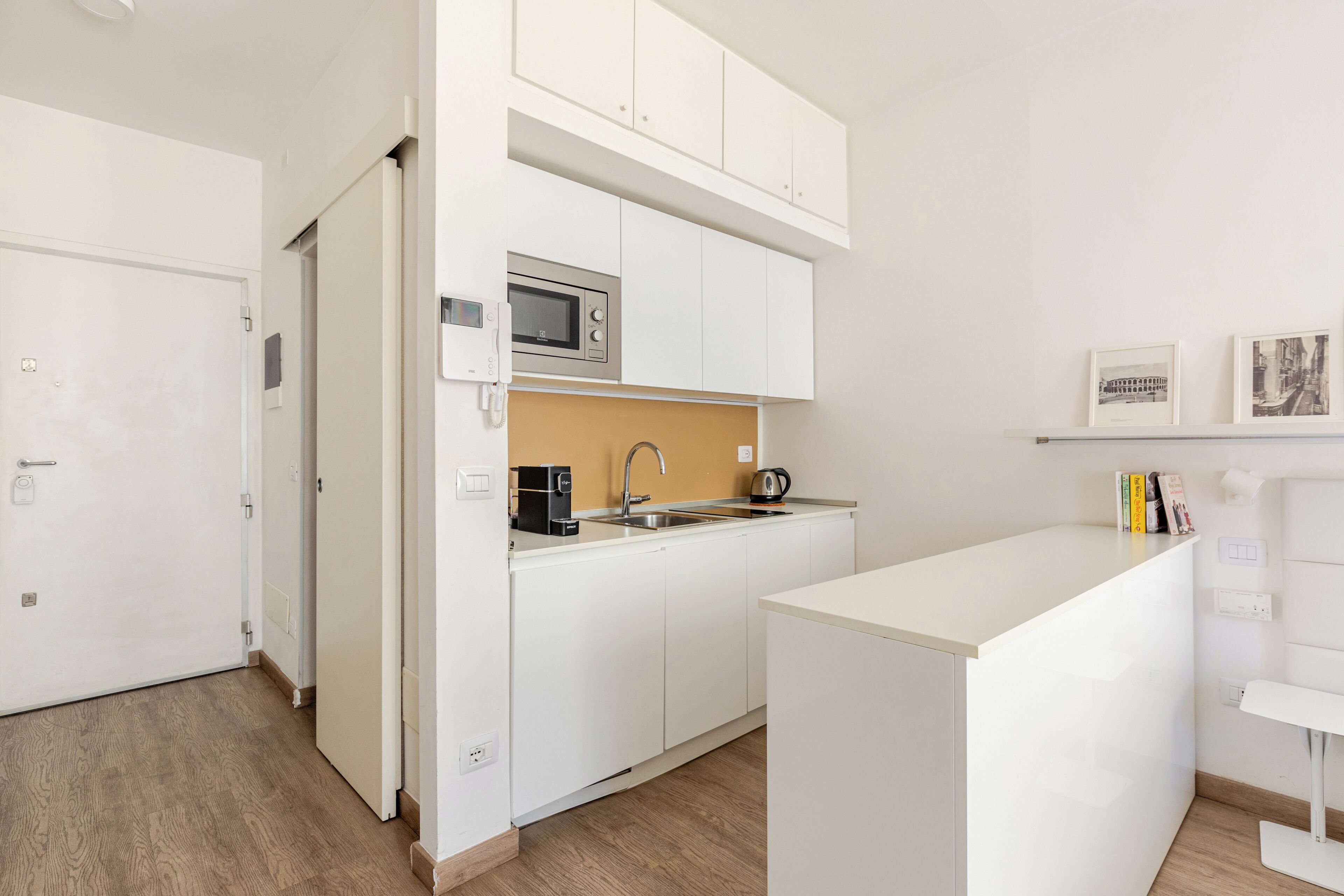 Cocina compacta con armarios blancos, microondas, lavamanos y una pequeña encimera.