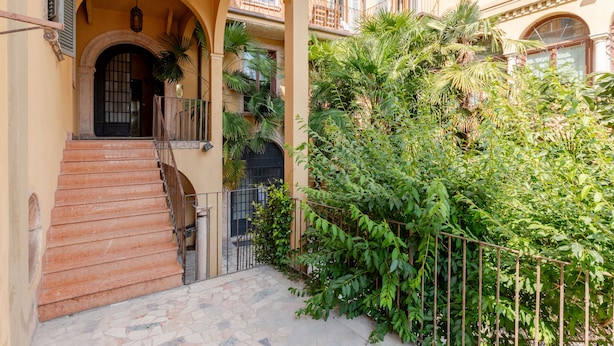 Un edificio con una escalera que lleva a la entrada, rodeado de vegetación y una valla metálica.
