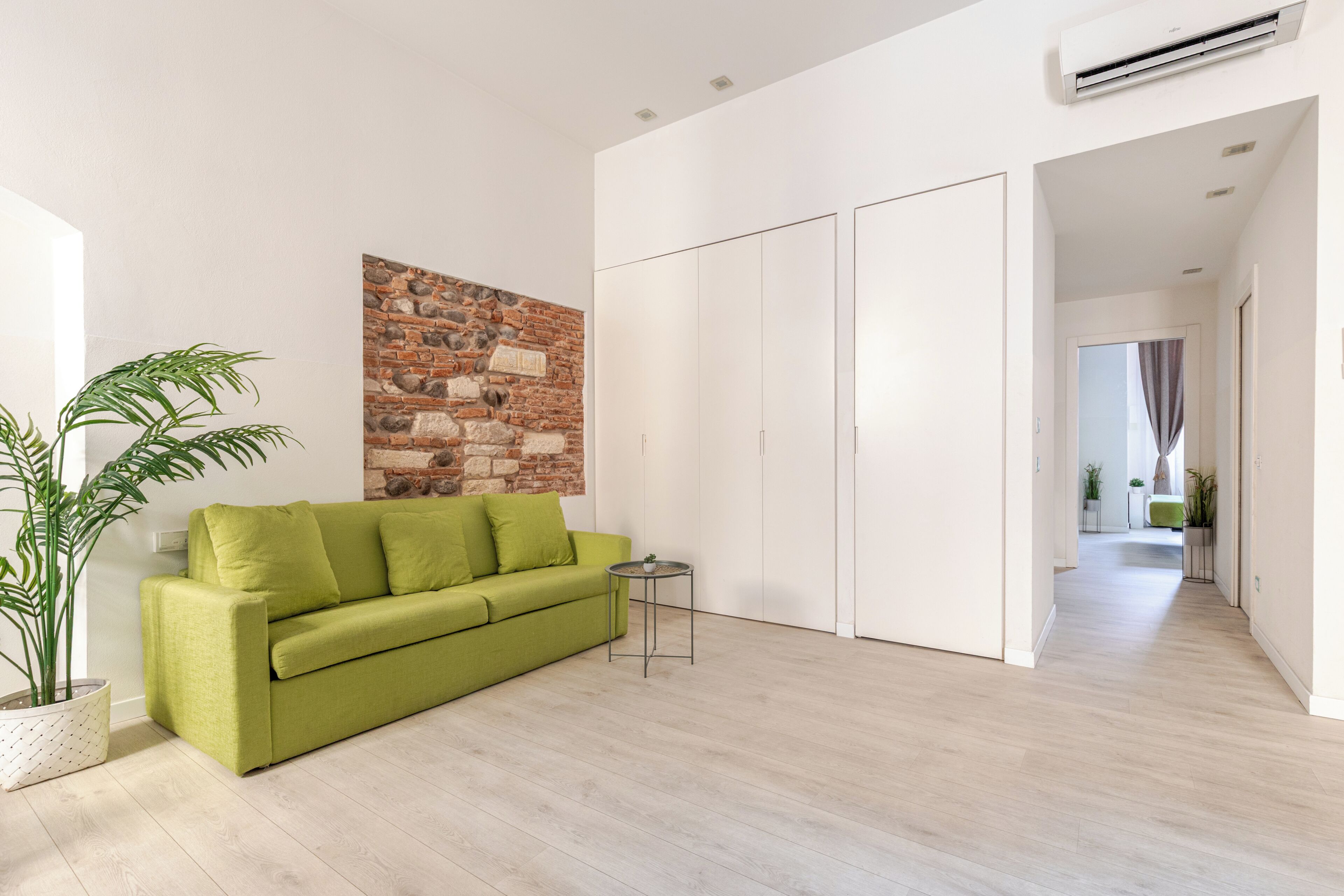 Un salon moderne avec un canapé vert, un mur en pierre et un couloir menant à une autre pièce.