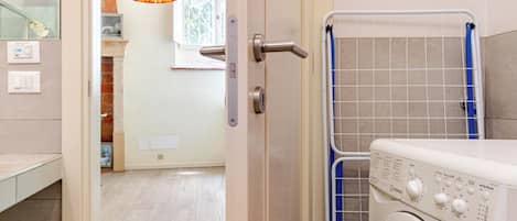 Uma área de lavanderia com máquina de lavar, varal e porta que dá para um espaço com teto de madeira e luminária pendente.