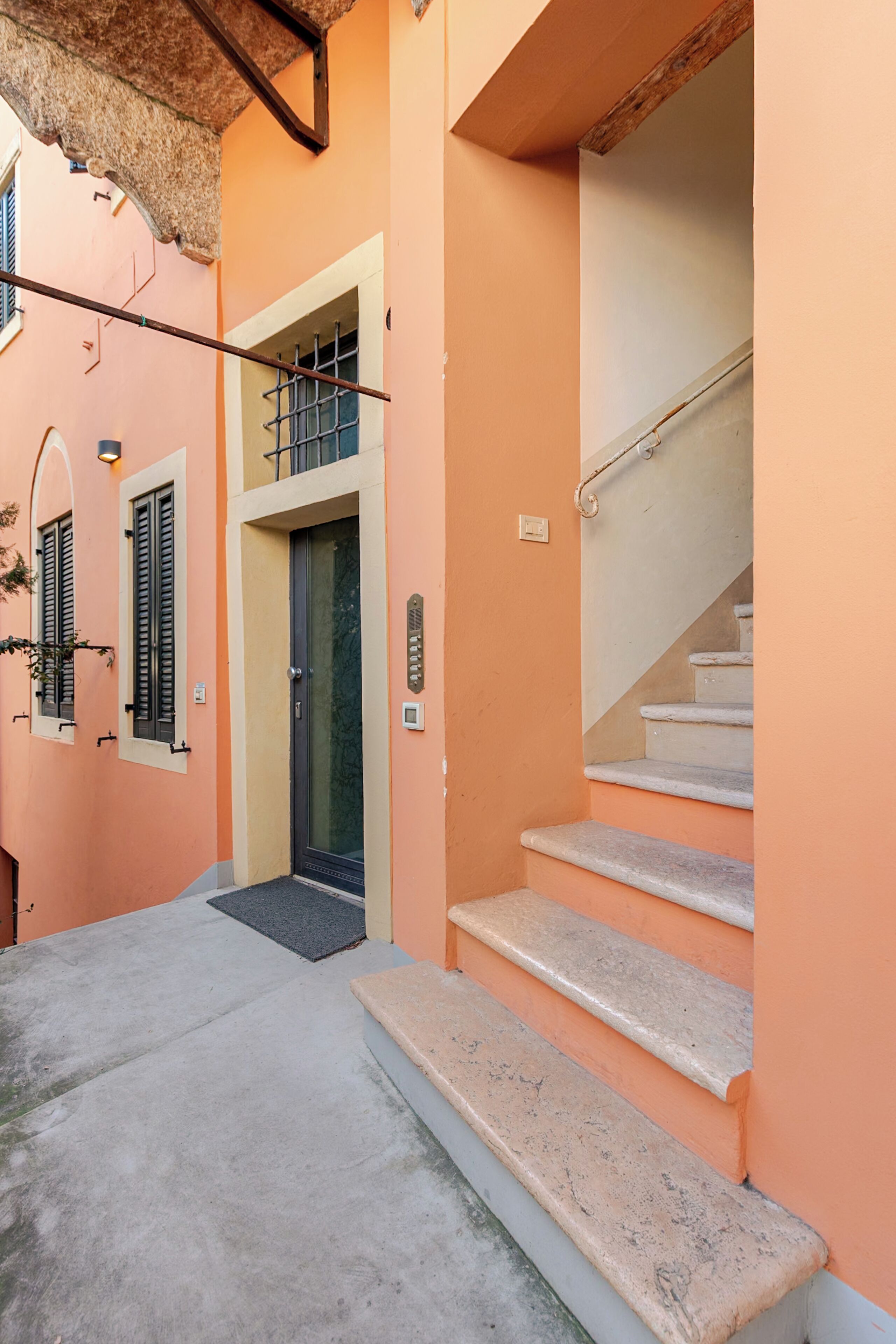 A narrow alleyway with a staircase leading to a door, a small outdoor area, and a building with a unique architectural design.