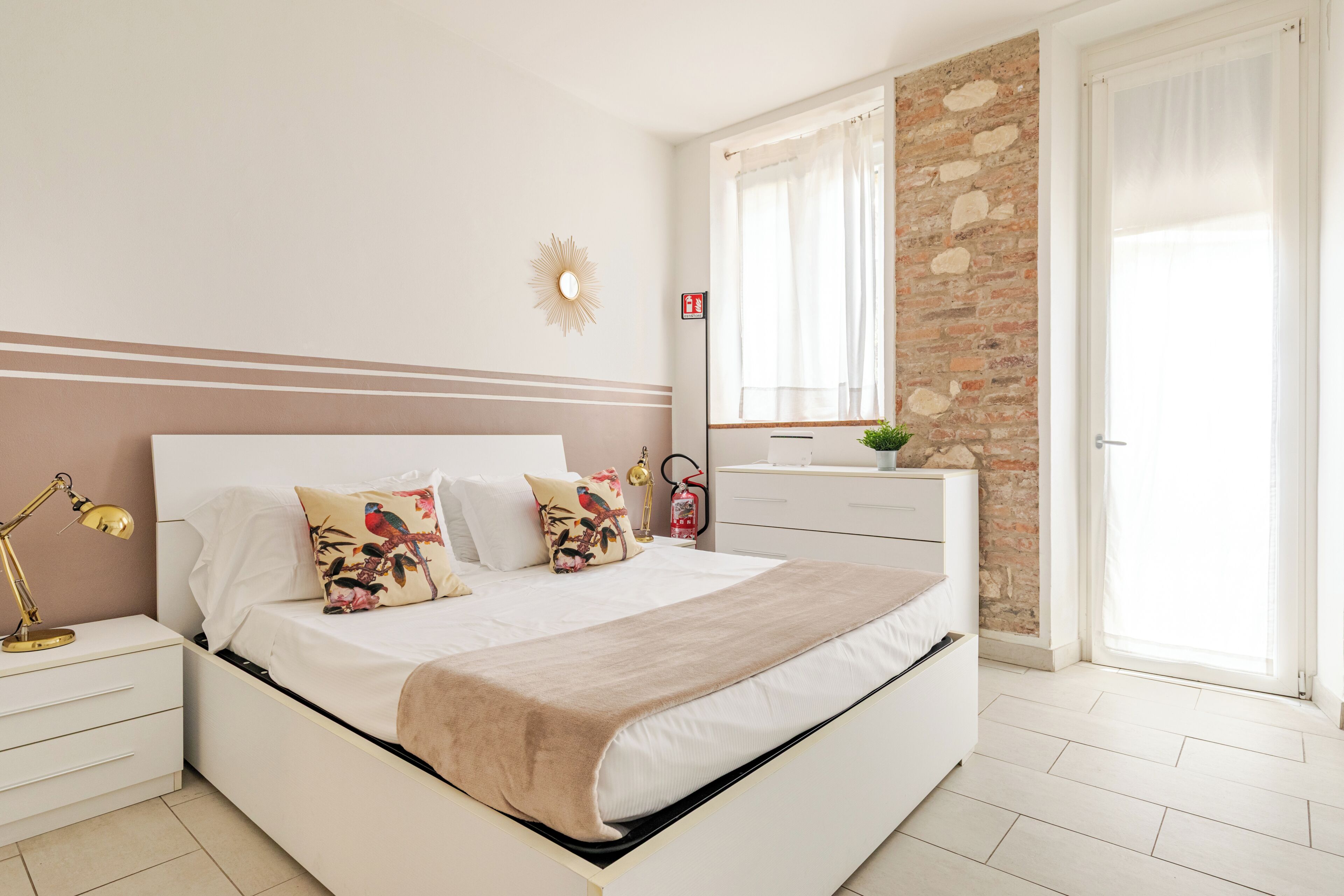 A bedroom with a bed, bedside table, lamp, and a brick wall.