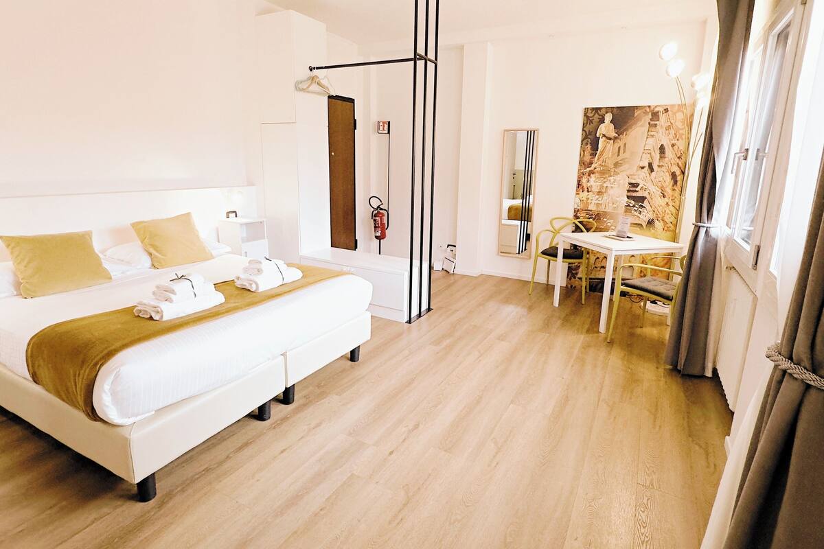 A hotel room with a bed, bedside table, and a small sitting area with a table and chairs.
