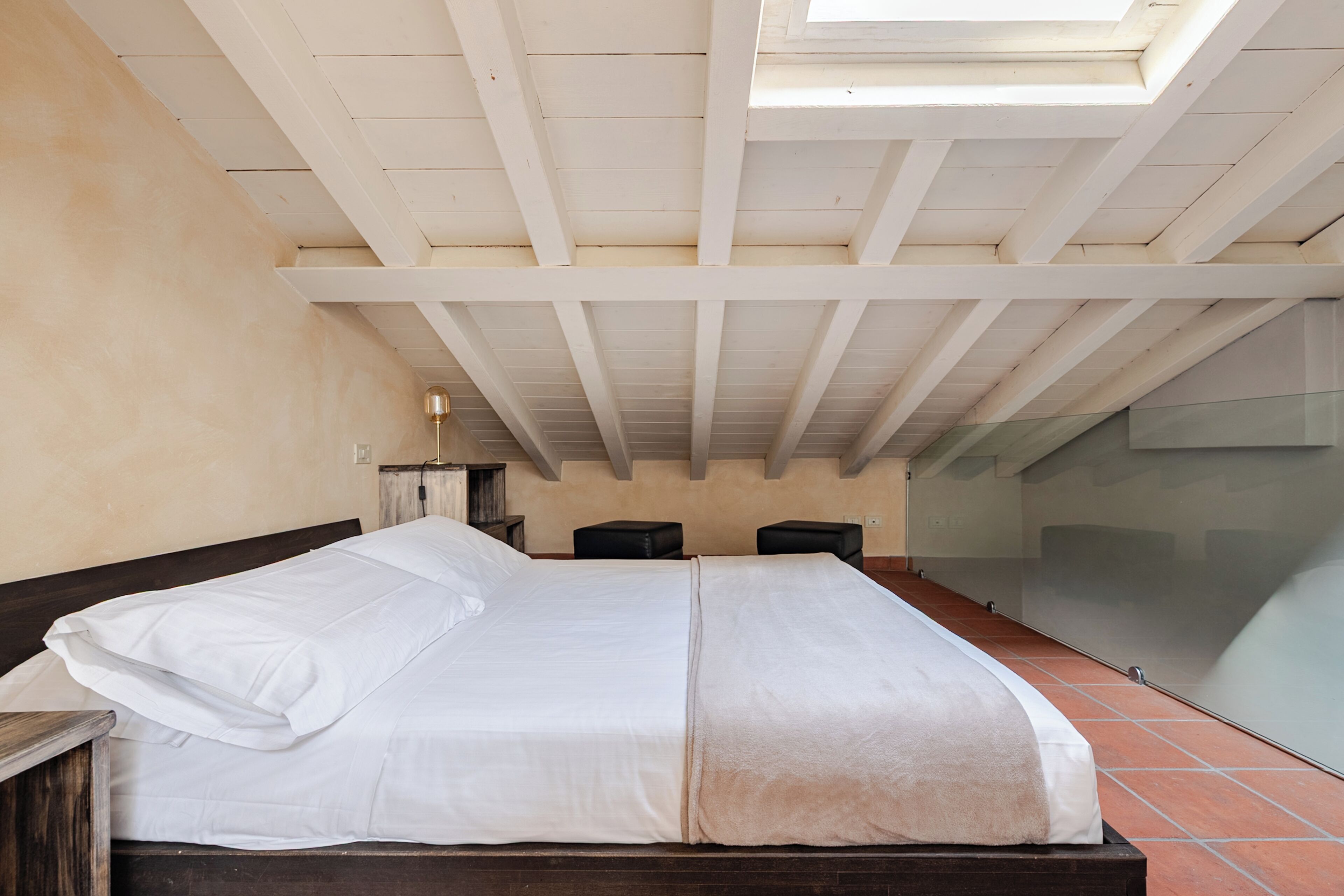 Un dormitorio con cama, mesita de noche, lámpara y tragaluz.