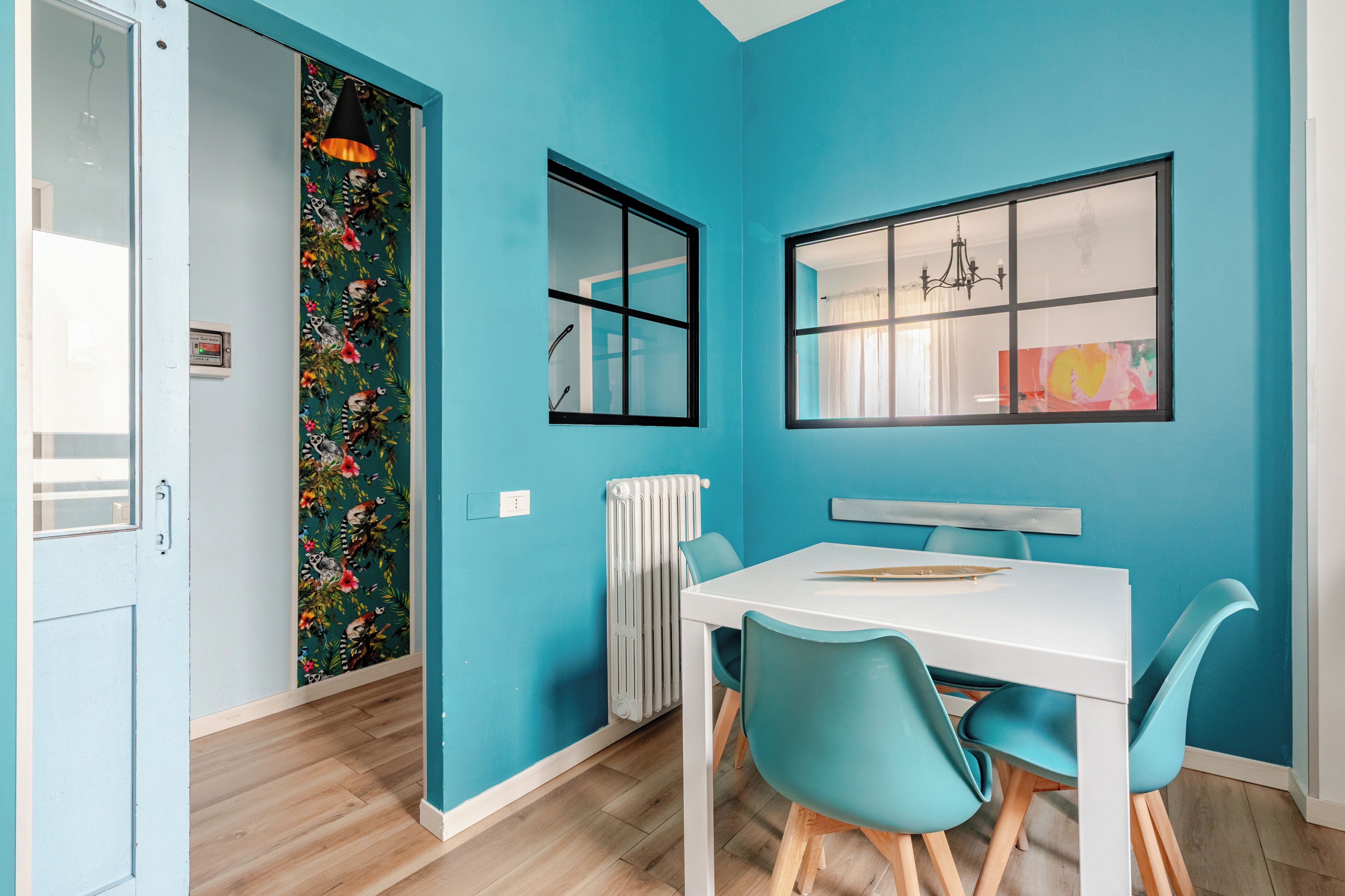 A room with teal walls, a white table, teal chairs, a window with a view, and a radiator.