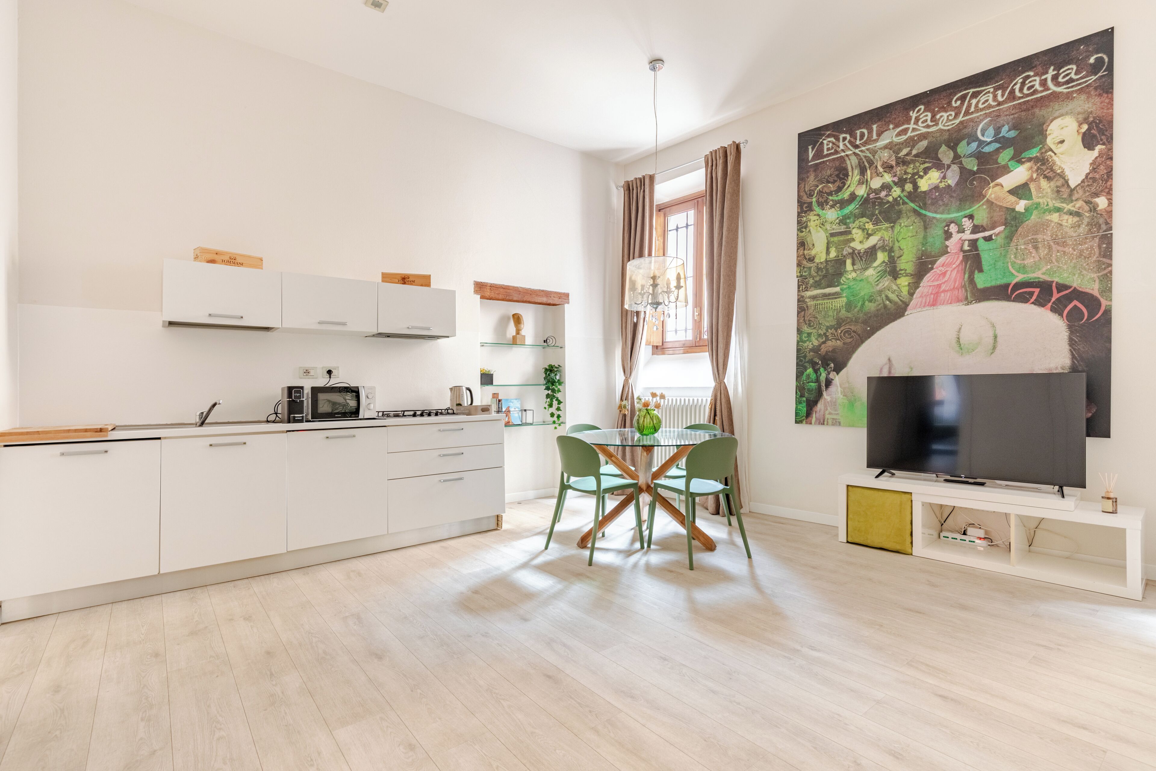 A modern kitchen with white cabinets, a dining table with chairs, a TV, and a large decorative painting.