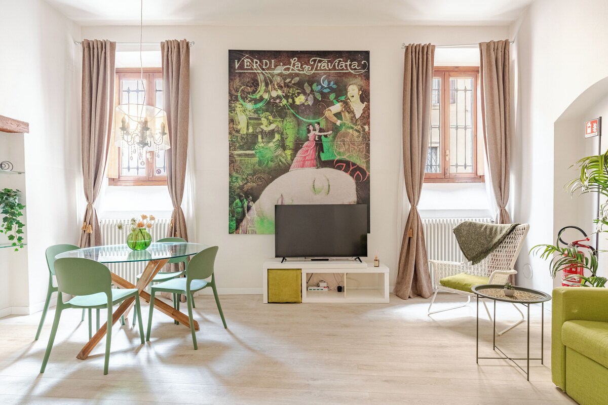 Una sala de estar con una mesa de vidrio, sillas verdes, un televisor de pantalla plana y un cartel grande en la pared.