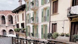 Un patio al aire libre con una mesa redonda y sillas, una cerca de metal, y edificios con contraventanas verdes y balcones al fondo.