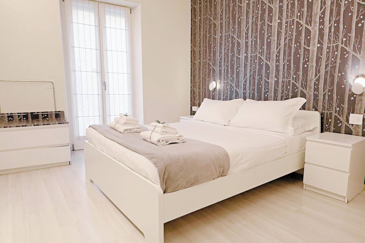 A modern bedroom with a bed, bedside tables, and a window.