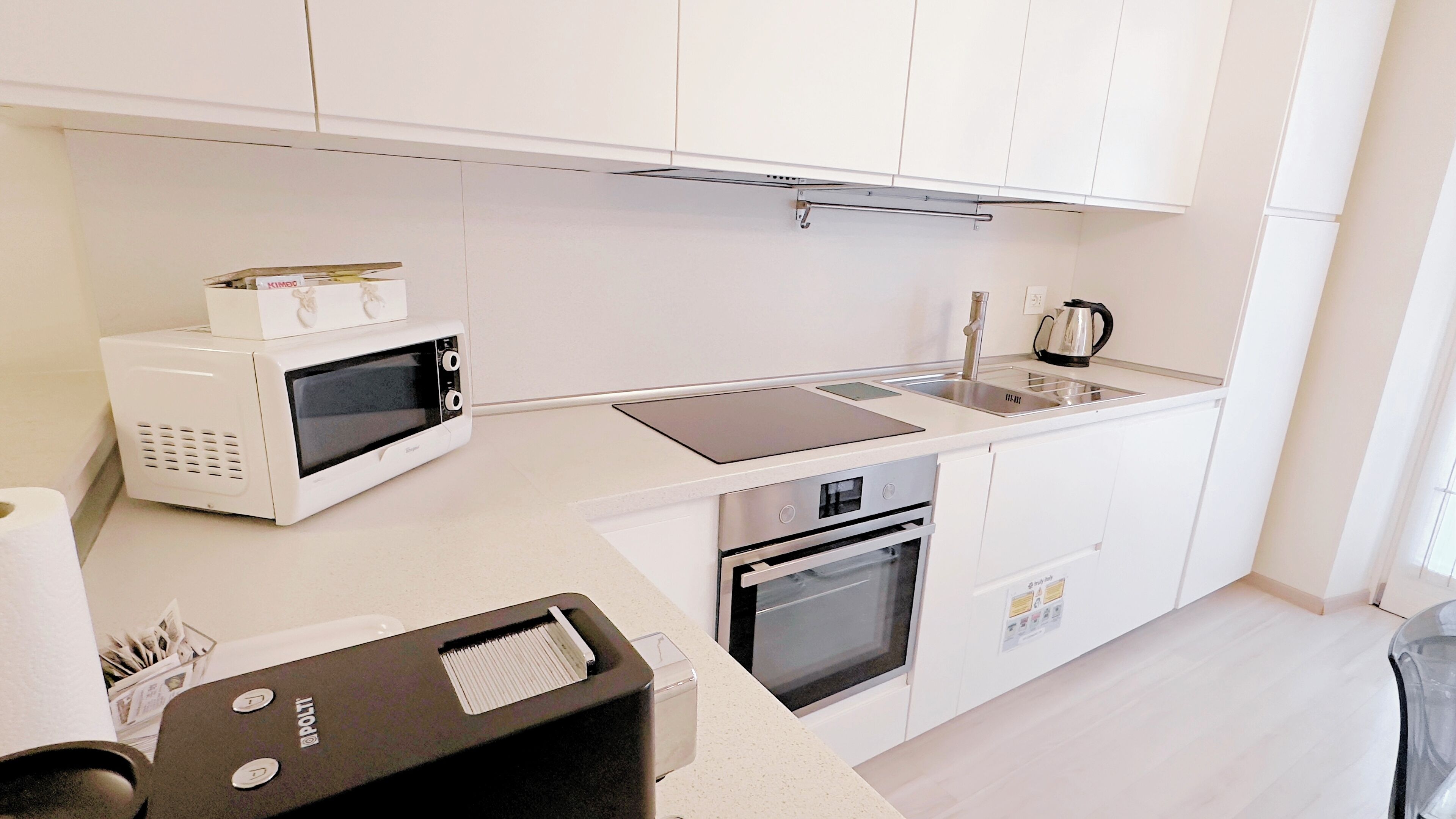 Eine kleine Küche mit weißen Schränken, einer eingebauten Mikrowelle, einem Wasserkocher und einem Toaster.