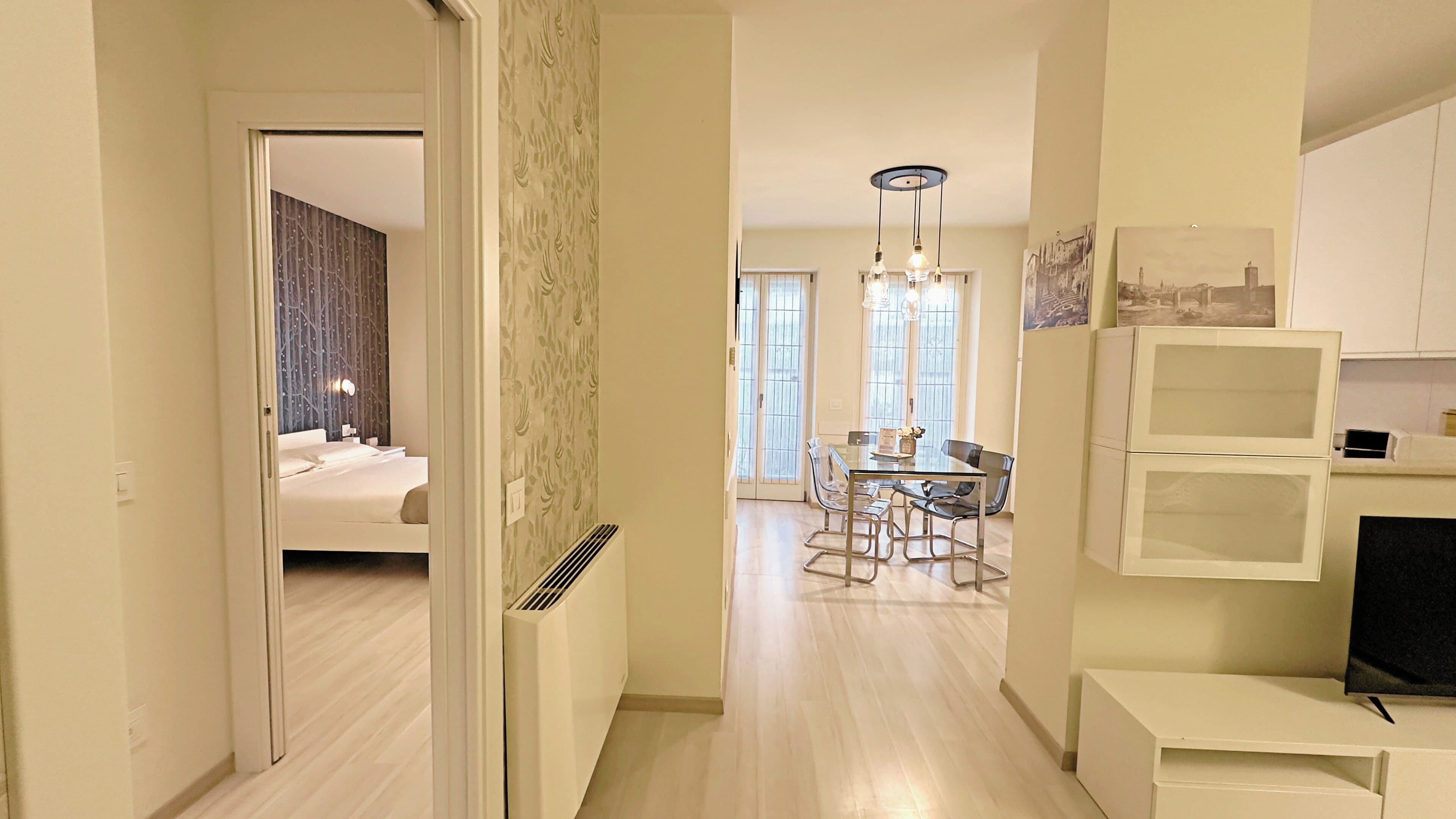 A modern hotel room with a bed, a desk, and a dining area with chairs and a table.
