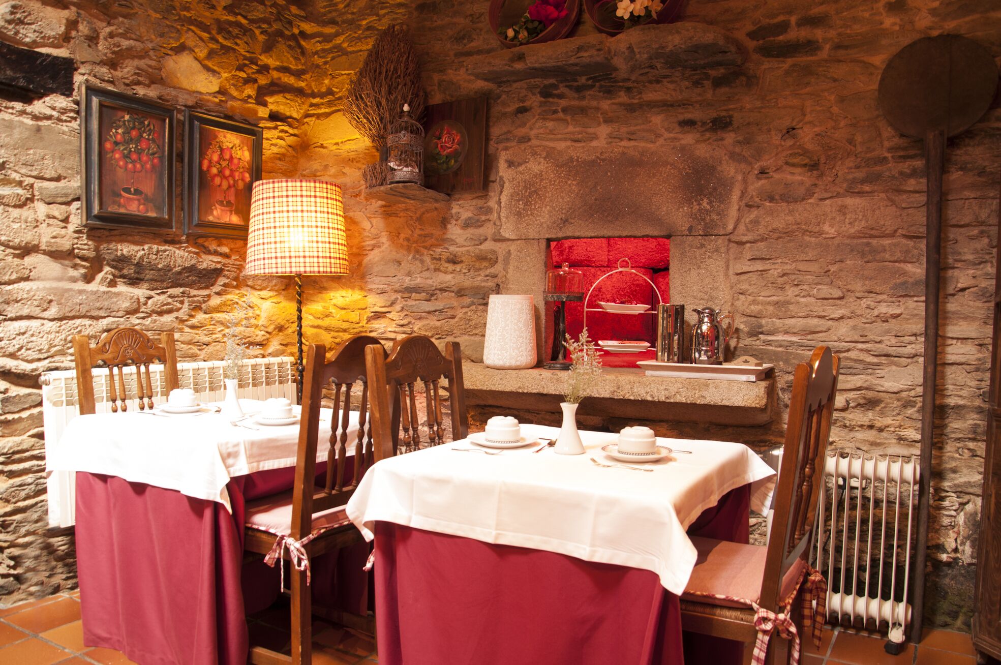 A stone-walled dining area with a table set for two, featuring a checkered tablecloth, white plates, and a red table runner.