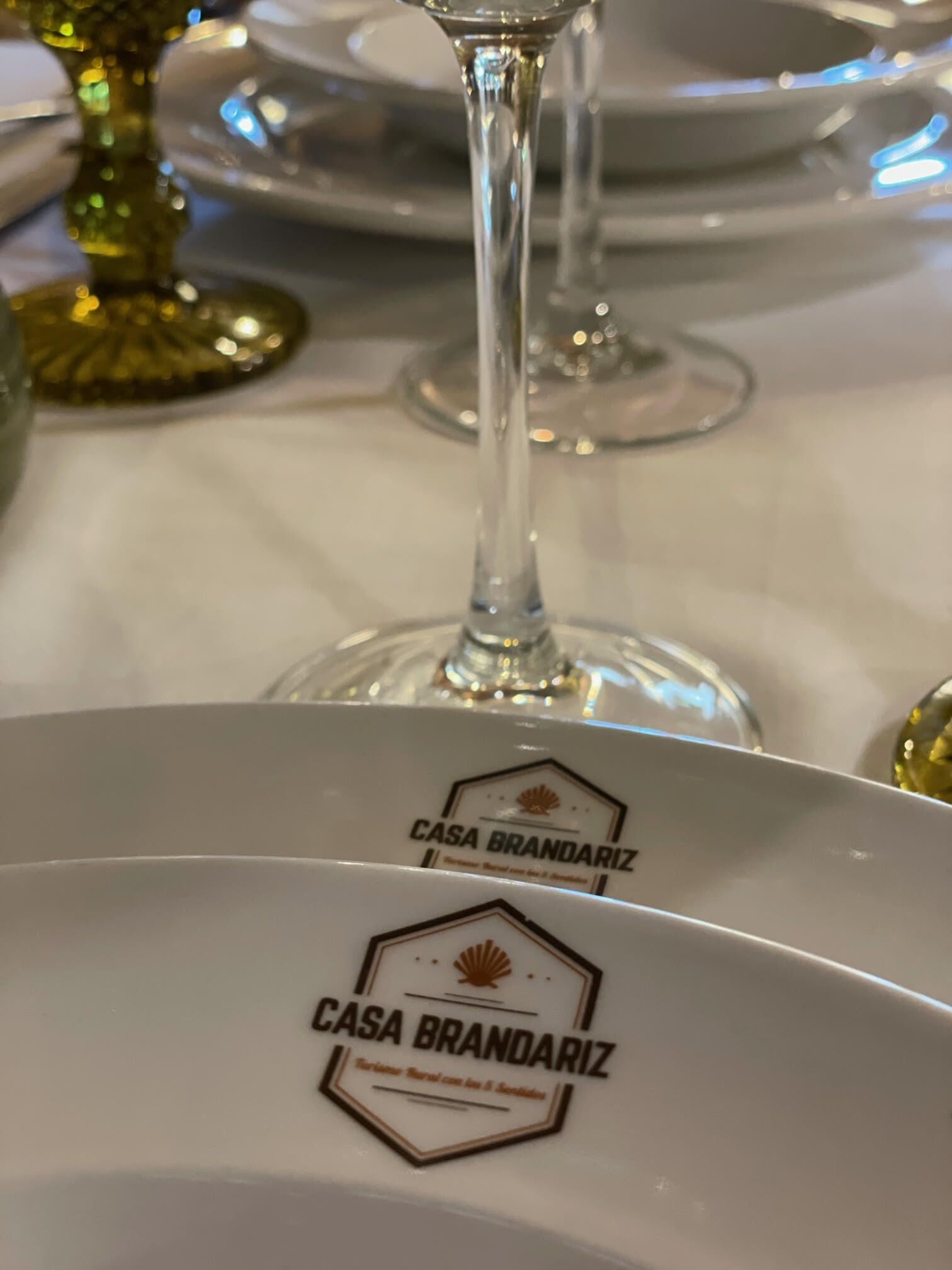 Una mesa de comedor con mantel blanco, una copa de vino de vidrio y un plato con el logotipo "CASA BRANDARIZ".