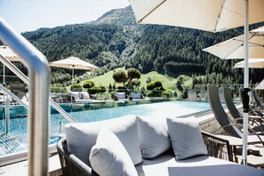Zona de piscina con sillones de descanso y sombrillas, con vistas a un paisaje montañoso.
