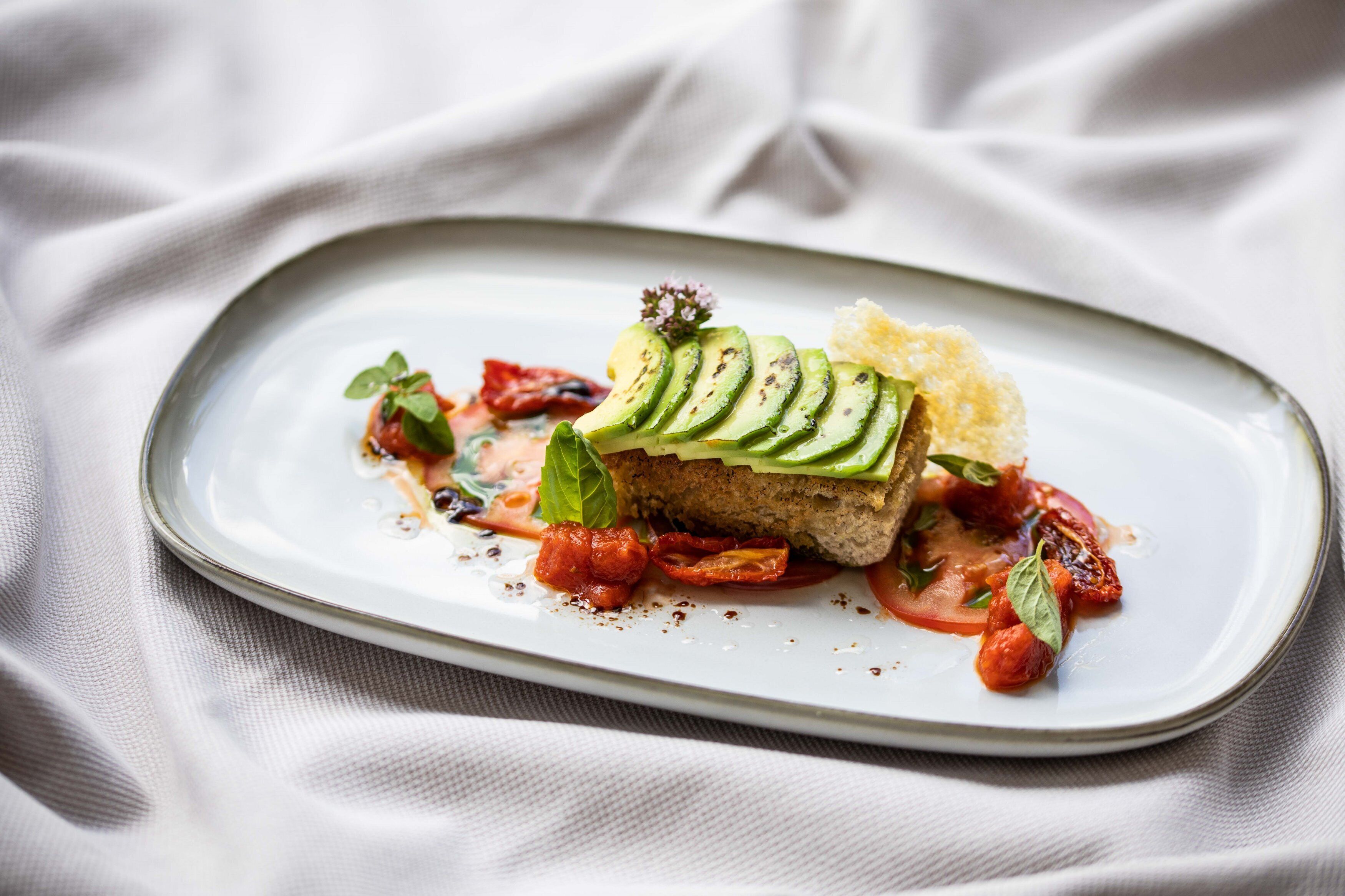 A plate with a sandwich, tomato slices, and basil leaves.