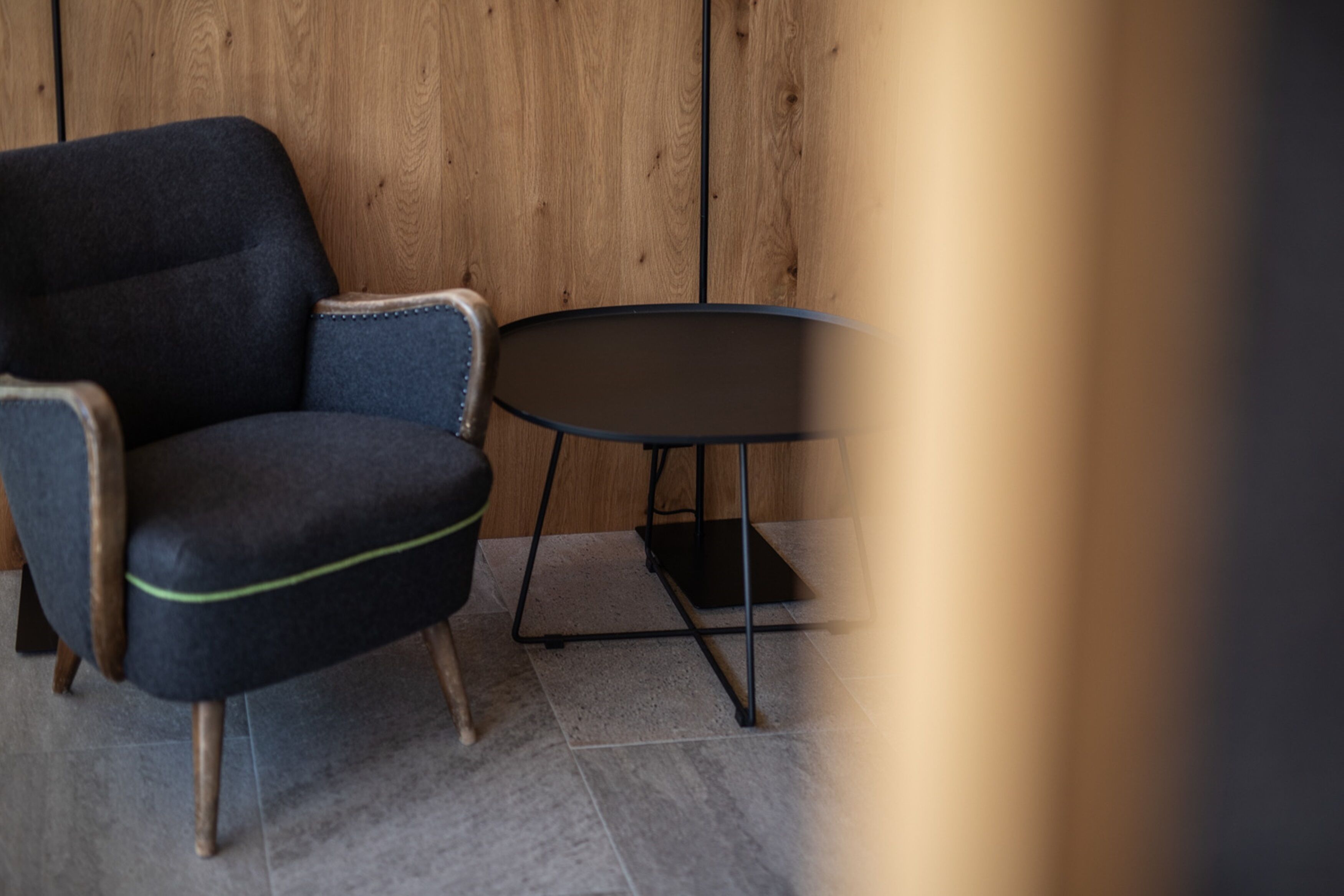 Una habitación moderna con un sillón azul oscuro, una pequeña mesa redonda y una pared de madera.
