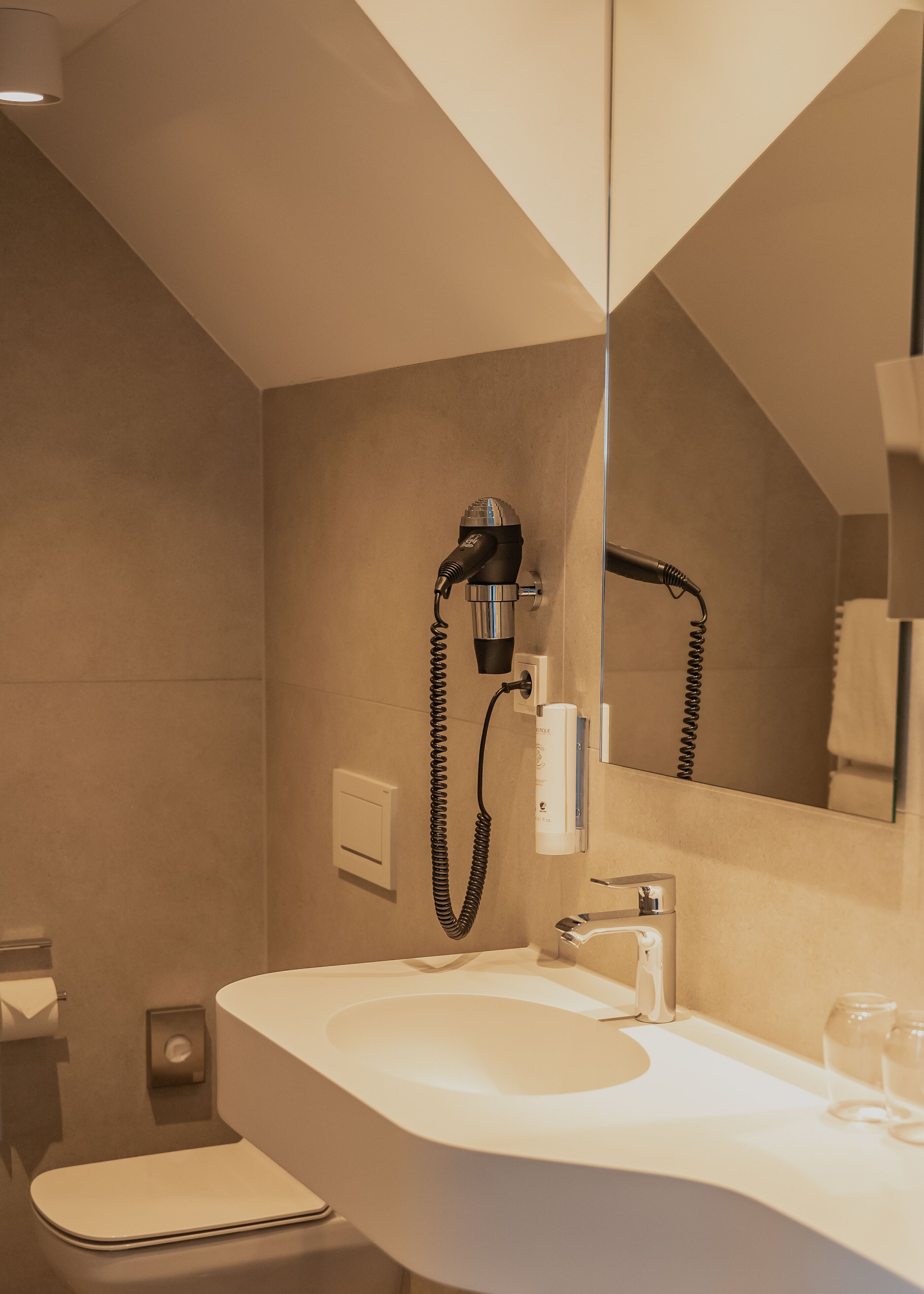 A modern bathroom with a large mirror, a sink, and a hairdryer mounted on the wall.
